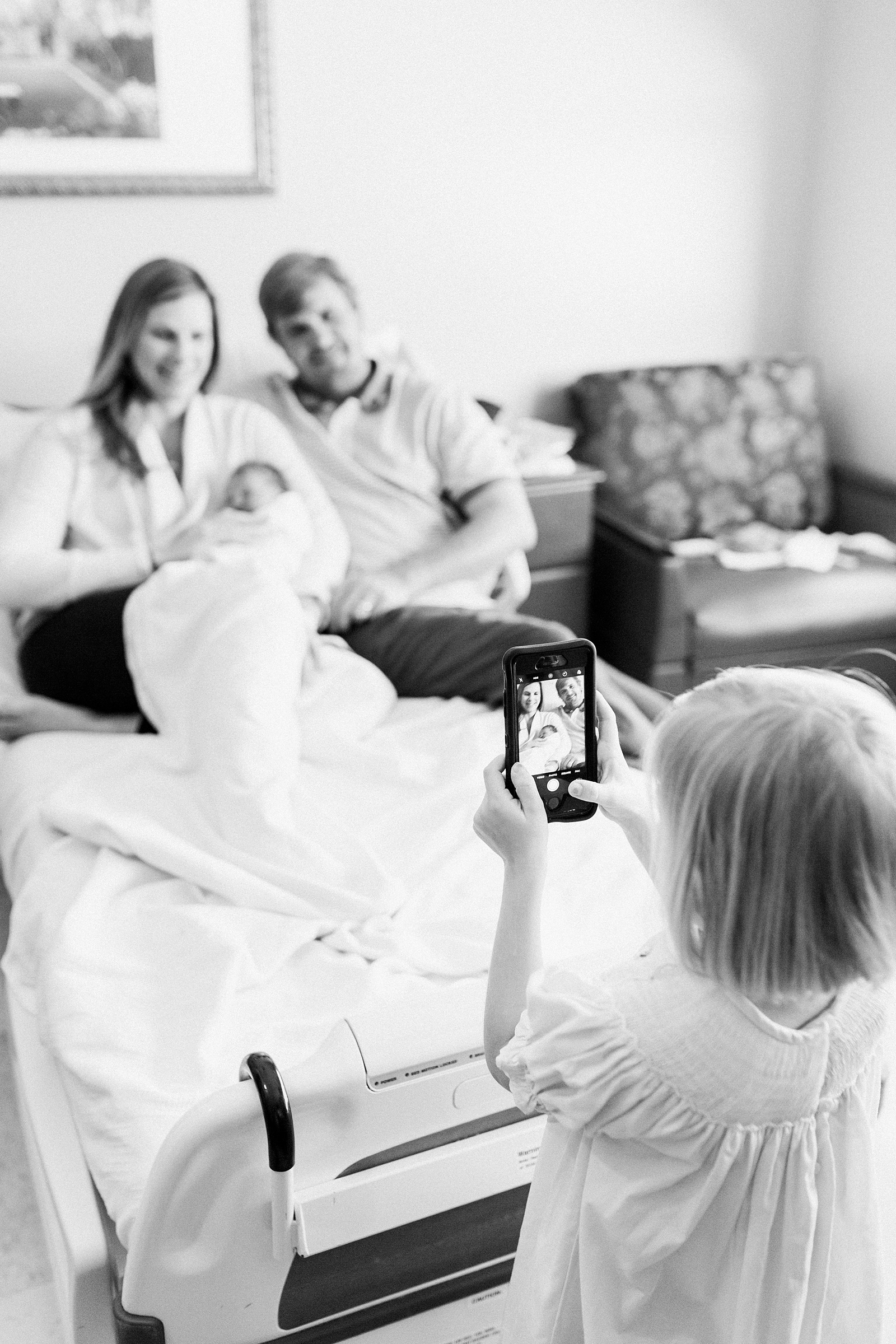 Candid moment of toddler taking photo of parents with new sister in Fresh 48 session by Caitlyn Motycka Photography 