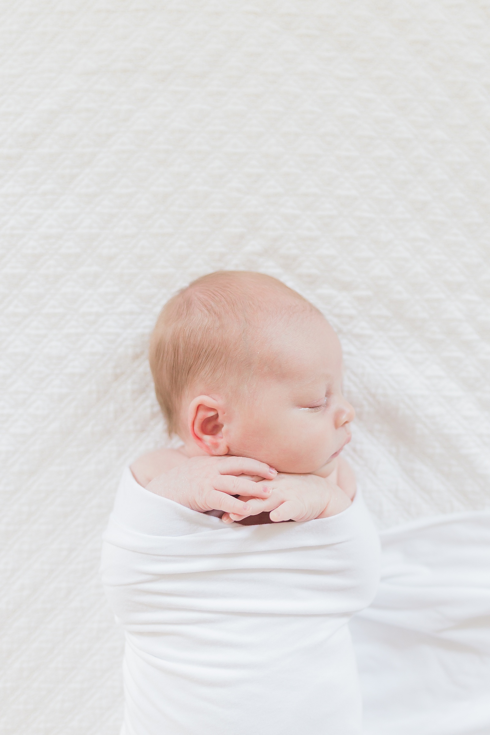 Baby in white swaddle during session by lifestyle newborn photographer, Caitlyn Motycka Photography