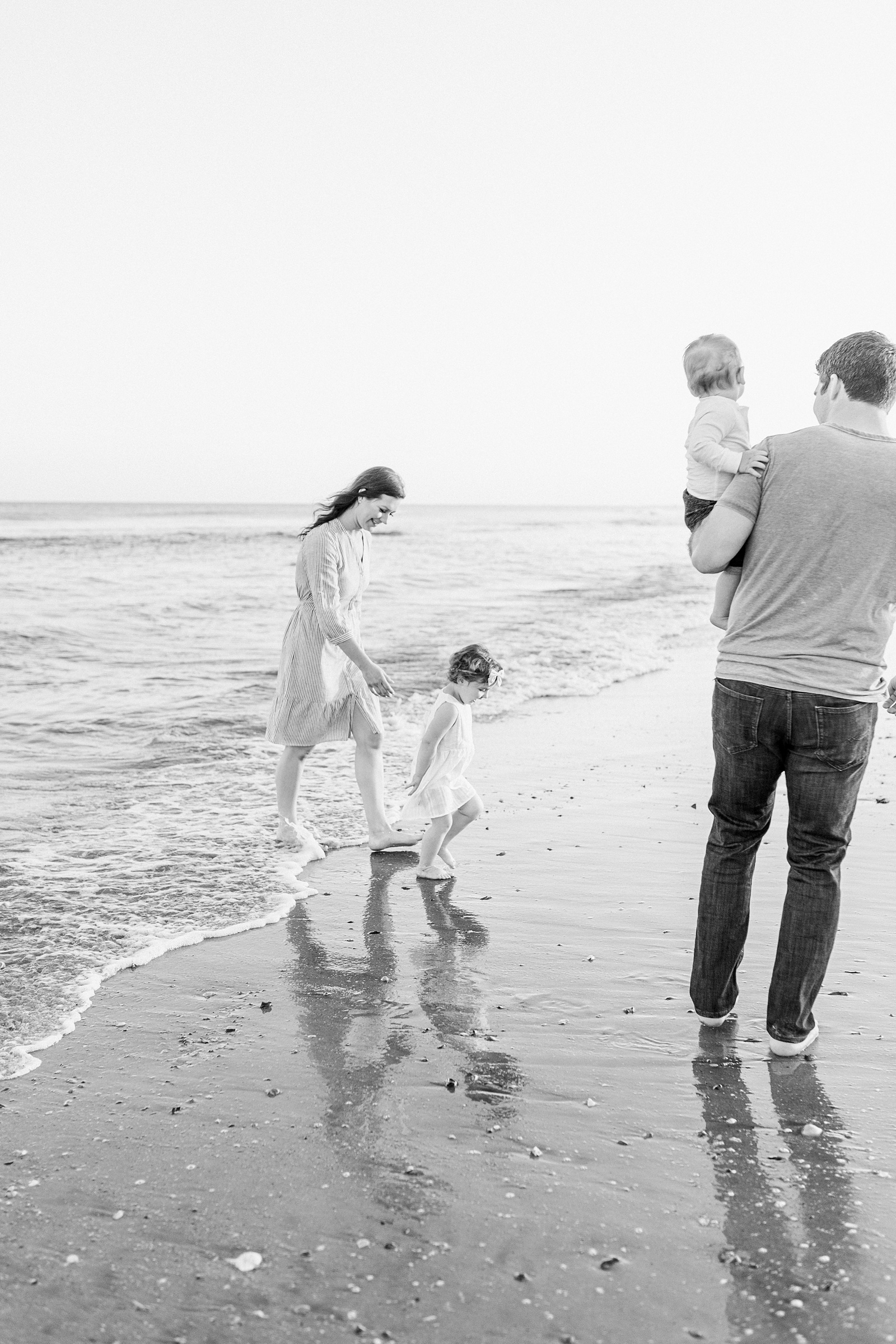 Black and white image of family playing in the water during family session on Isle of Palms beach | Caitlyn Motycka Photography
