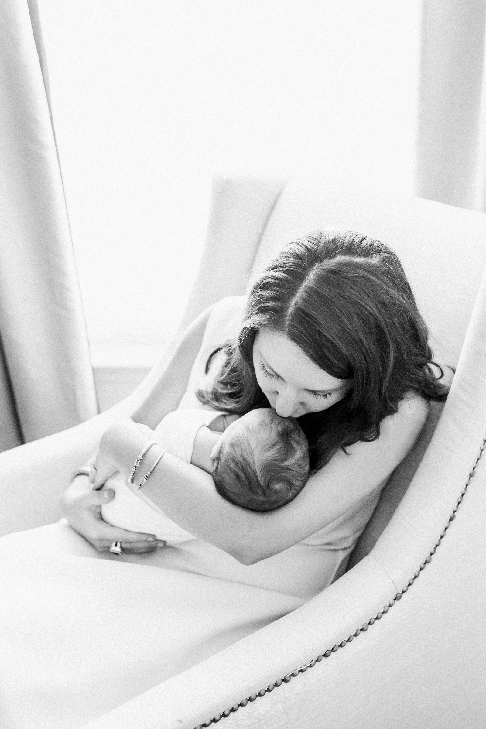 Black and white image of mom kissing baby in rocker of nursery by Caitlyn Motycka Photography