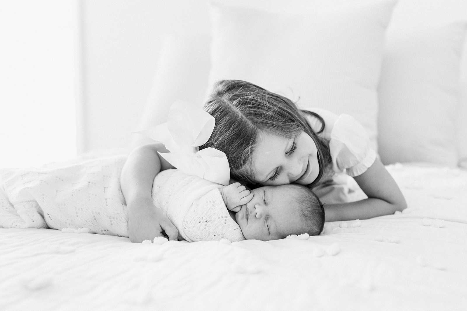Black and white image of big sister on bed with newborn during lifestyle newborn session by Caitlyn Motycka Photography