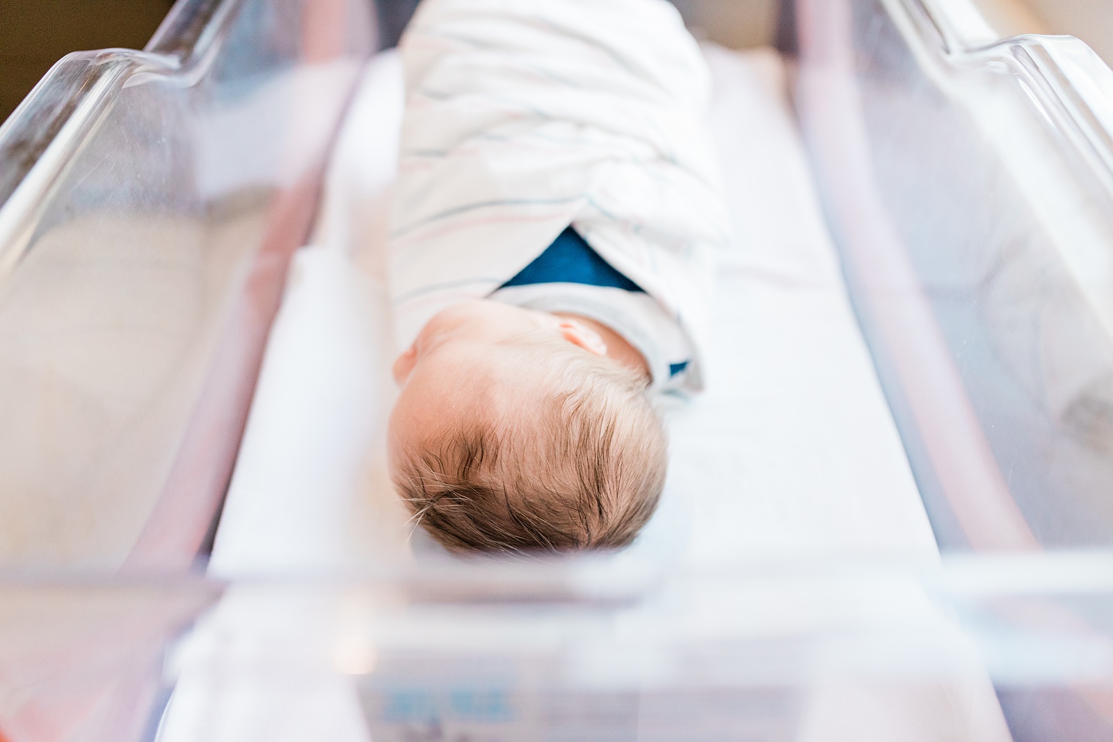 Baby with head of hair in hospital bassinet by Caitlyn Motycka Photography