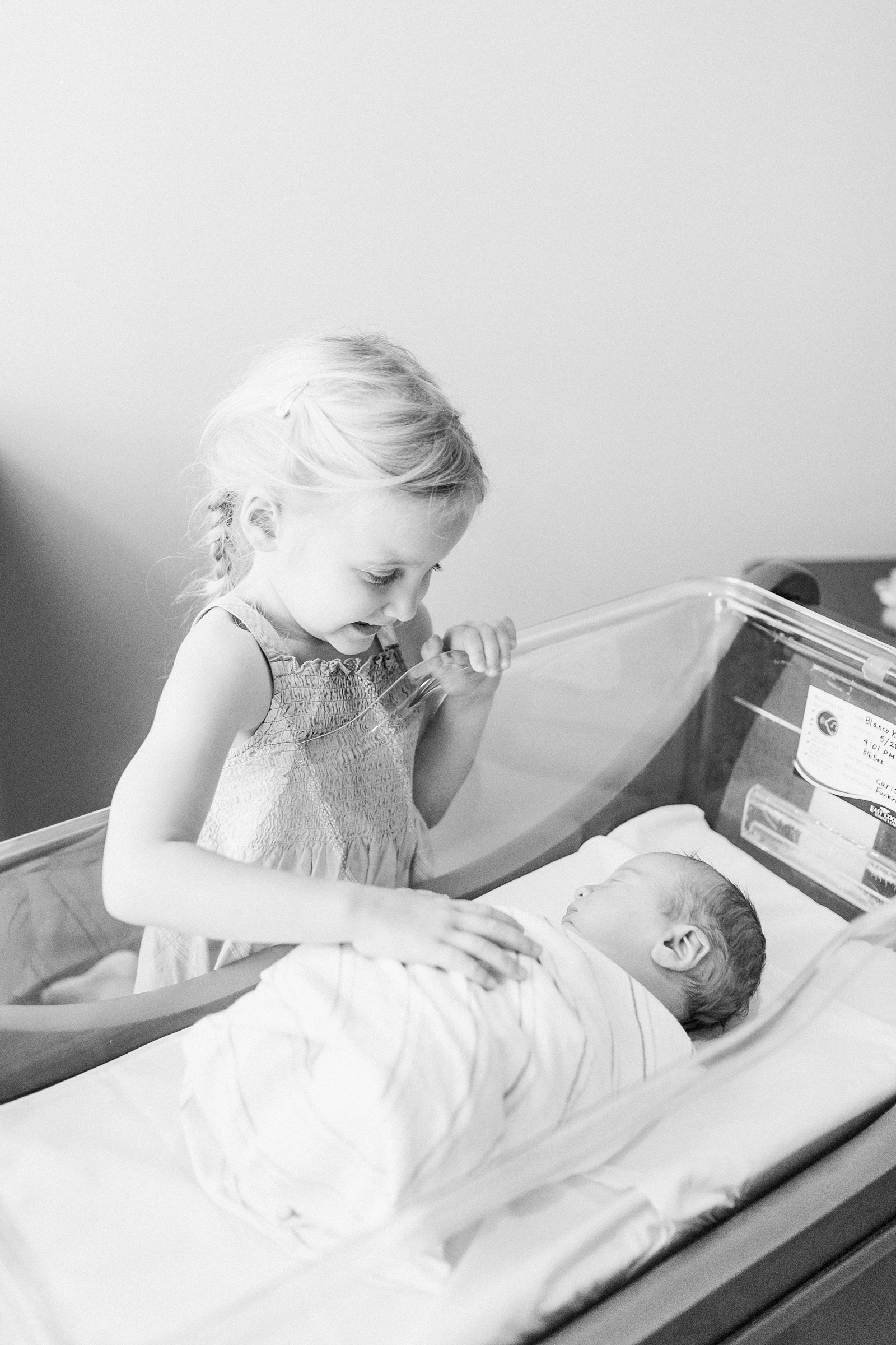 Black and white image of sister greeting baby brother in the hospital by Caitlyn Motycka Photography