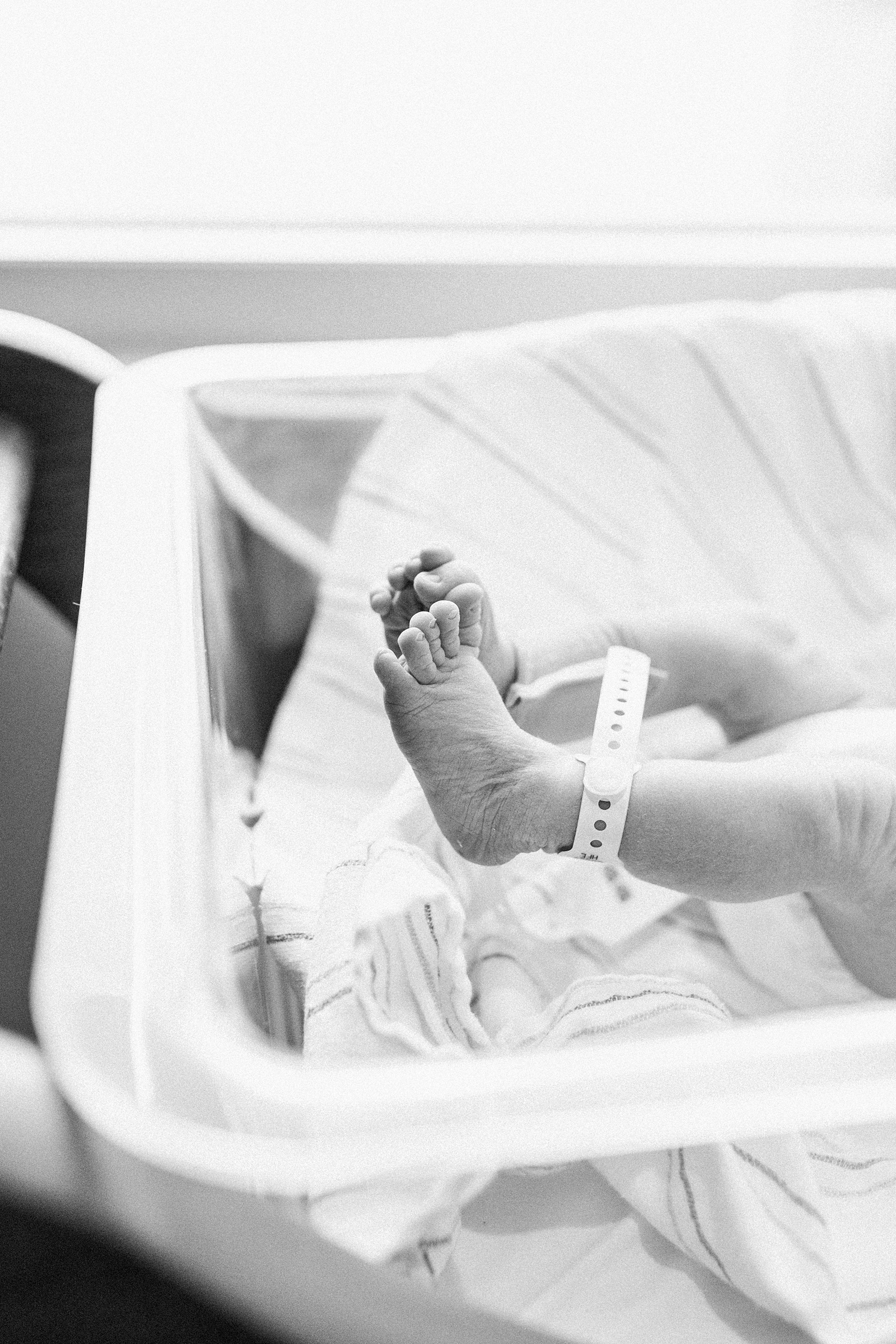 Black and white image of newborn feet in hospital bassinet | Caitlyn Motycka Photography