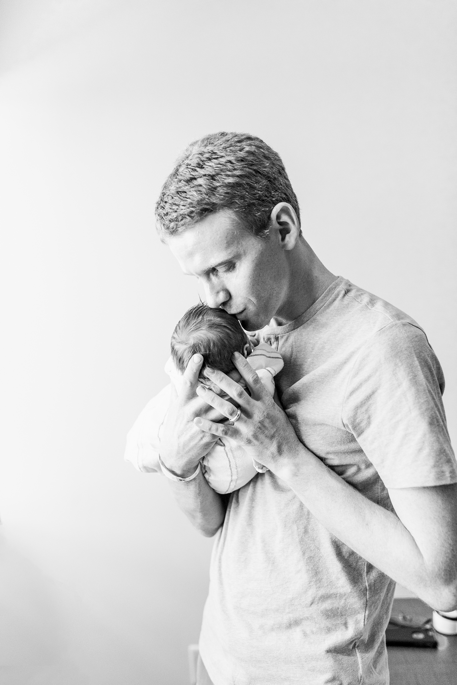 Black and white image of Dad kissing baby in hospital | Caitlyn Motycka Photography