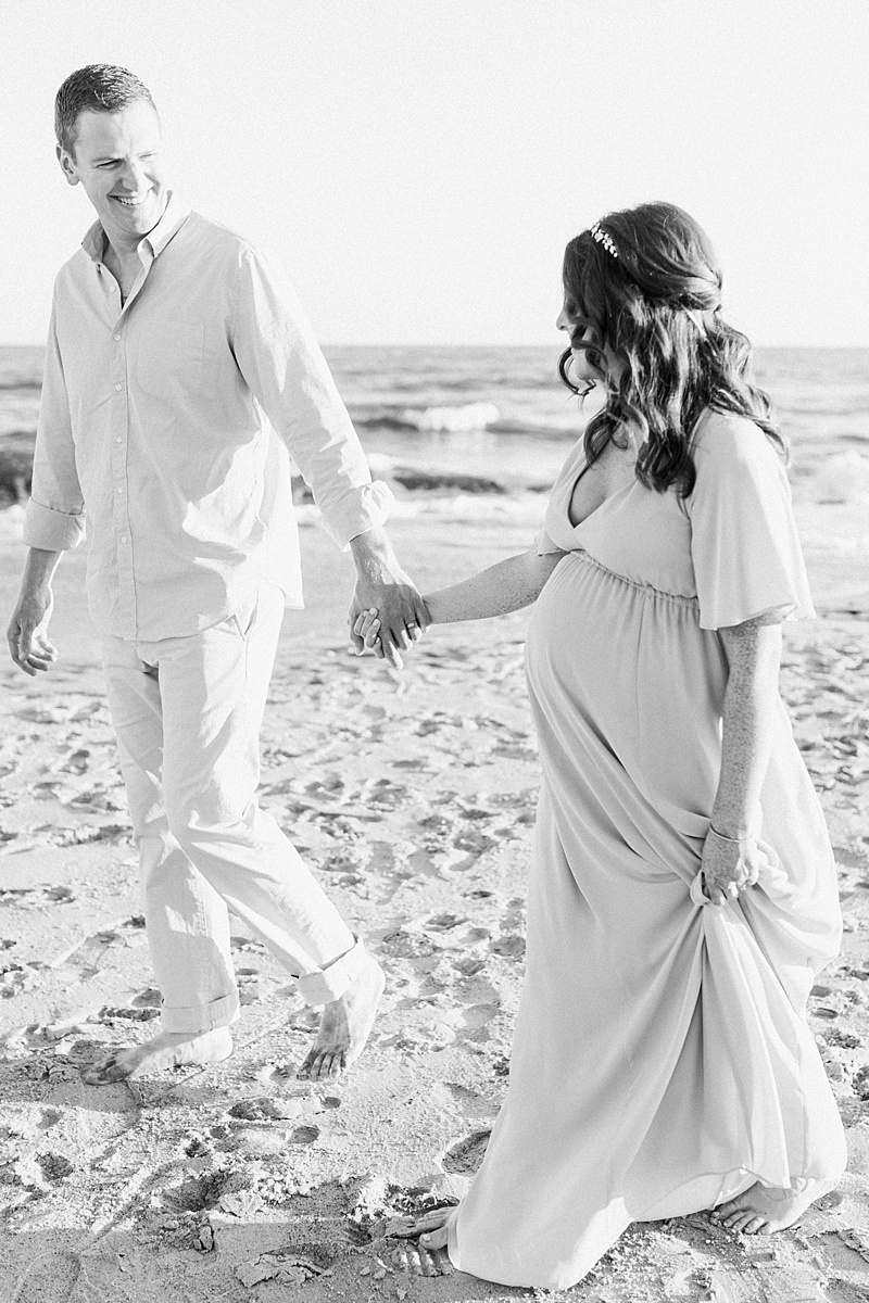 Black and white photo of the parents-to-be walking on the beach during maternity session on IOP | Caitlyn Motycka Photography.