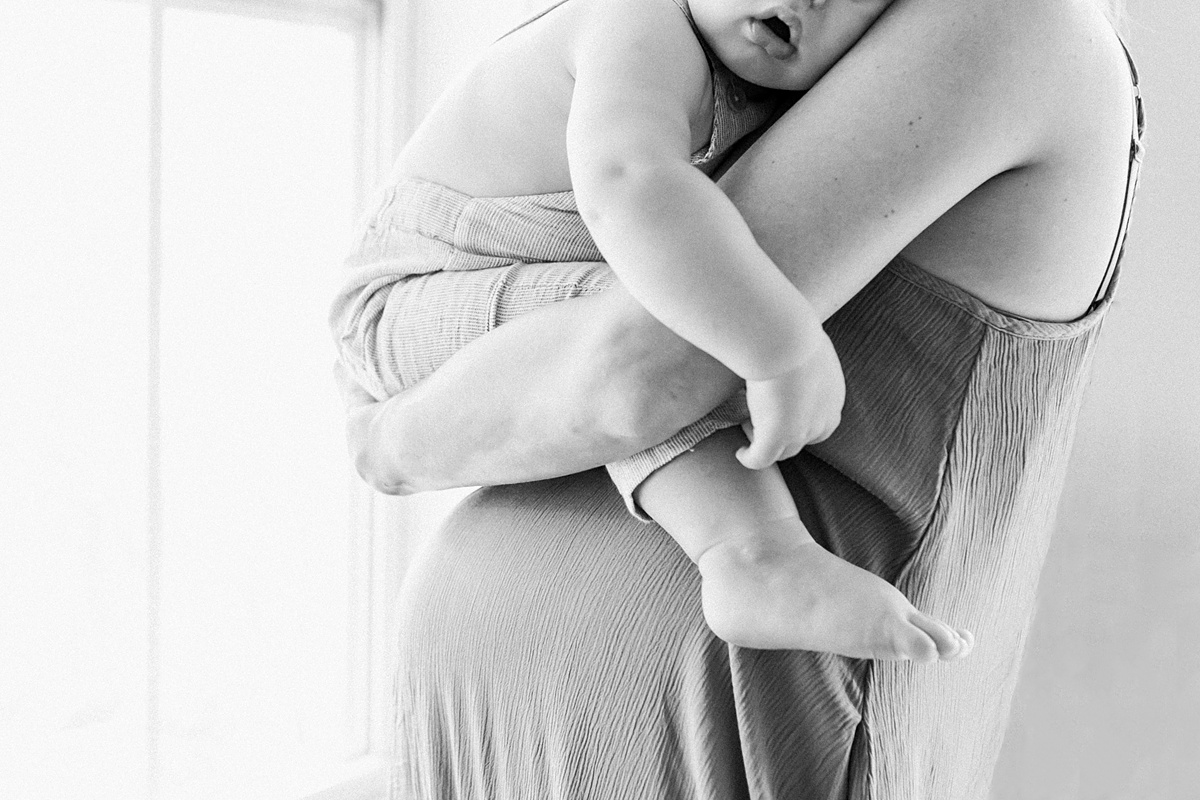Black and white photo of Mom holding toddler on bump during In-home lifestyle maternity session by Caitlyn Motycka Photography