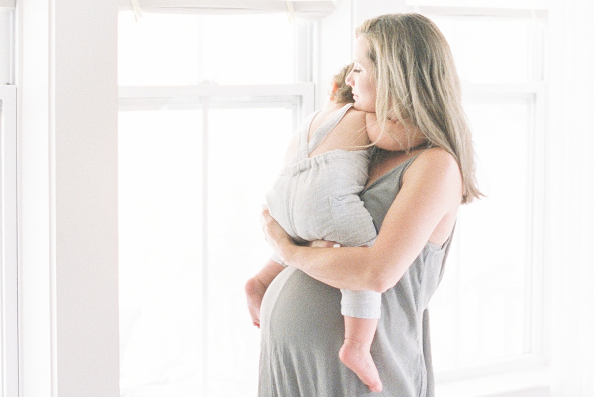 Film image ofd Mom holding toddler on bump during In-home lifestyle maternity session by Caitlyn Motycka Photography