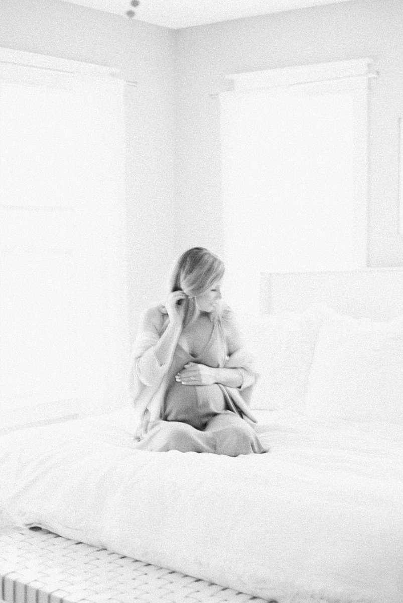 Black and white film image of mom with bump on bed during in-home lifestyle maternity session | Caitlyn Motycka Photography