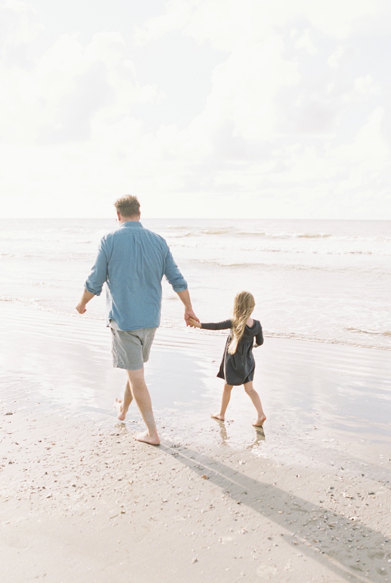 Father, daughter walk on Folly Beach during family photoshoot with Caitlyn Motycka Photography. 