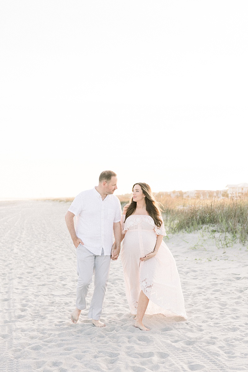 Mama and Dad to twin boys walking on the beach during pregnancy photoshoot. Photos by Charleston Newborn Photographer, Caitlyn Motycka Photography. 