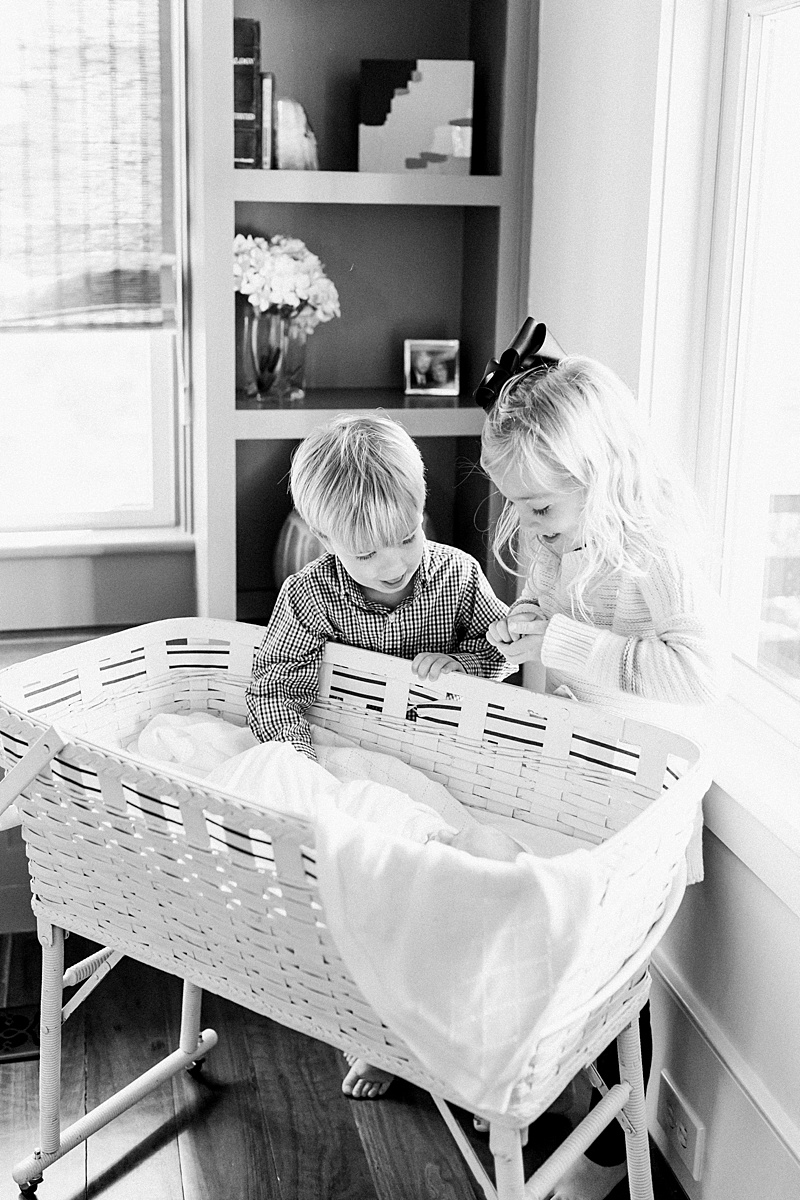 Black and white photo of siblings and baby brother in Moses basket in the Clients' Daniel Island home. Photos by Daniel Island Newborn Photographer, Caitlyn Motycka Photography. 