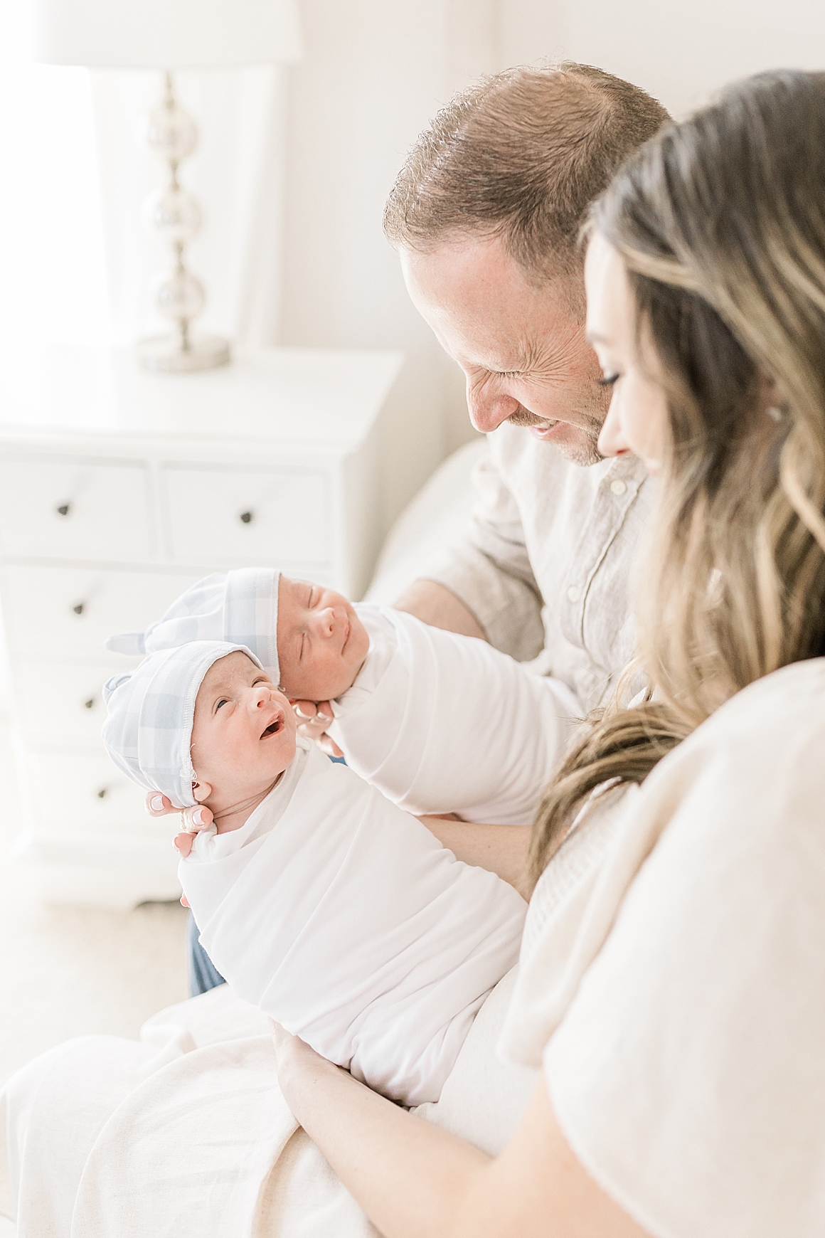 Mom and dad holding twin boys with blue and white gingham baby hats and white copper pearl swaddles. Photos by Caitlyn Motycka Photography.