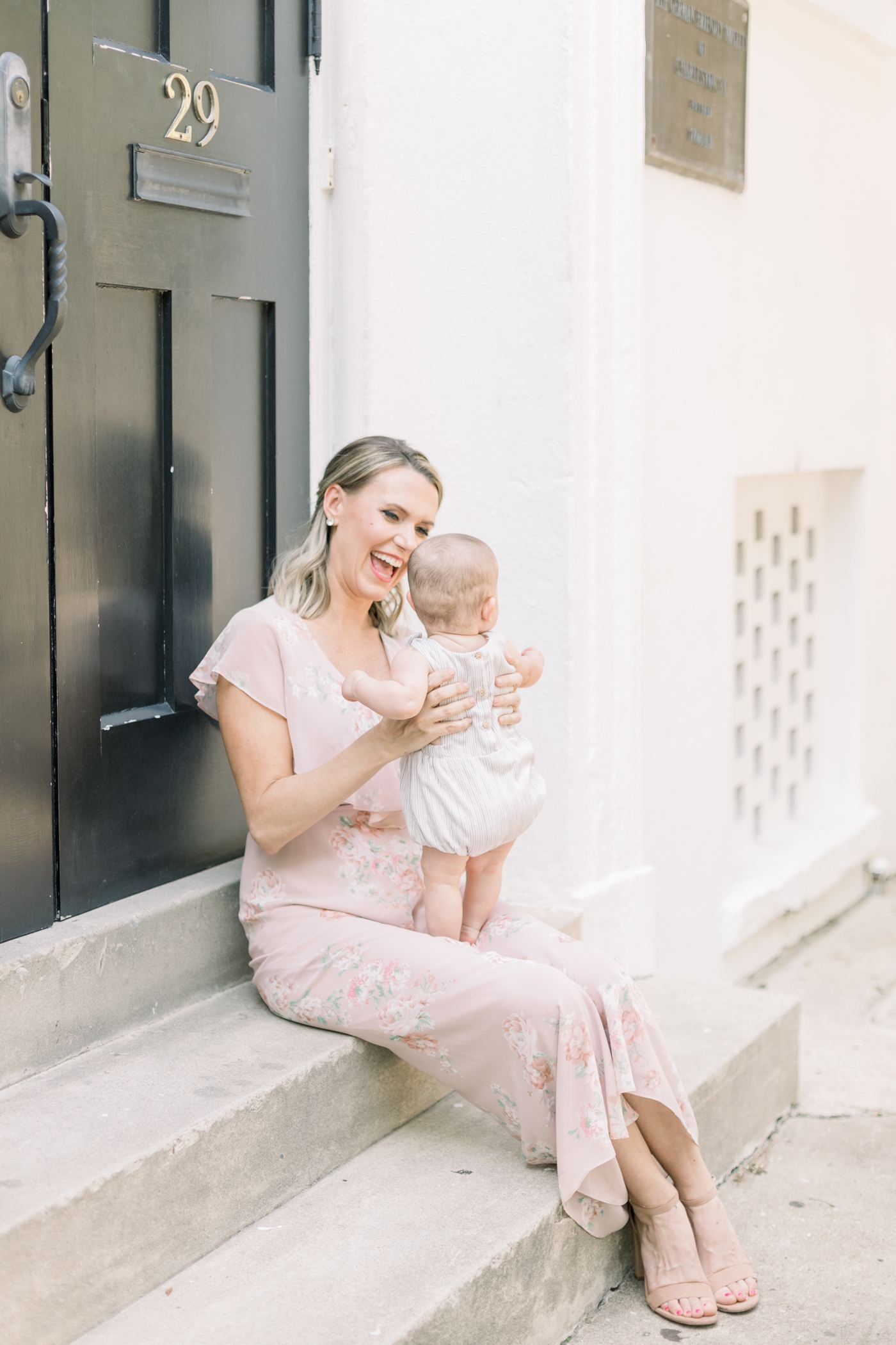 Mom smiling at baby while sitting on steps in historic district of Charleston. Photo by Caitlyn Motycka Photography.
