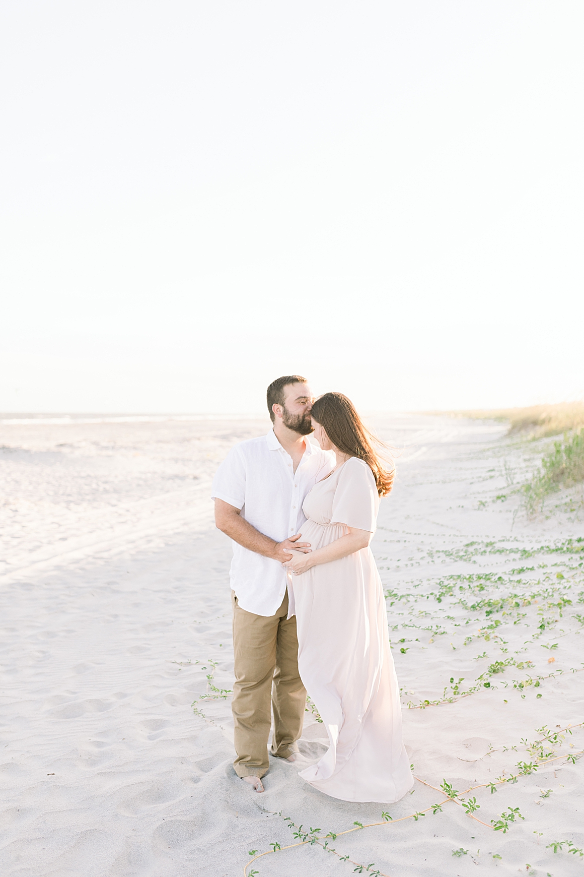 Husband kissing wife on the forehead during maternity session on the beach in Charleston, SC. Photos by Caitlyn Motycka Photography. 