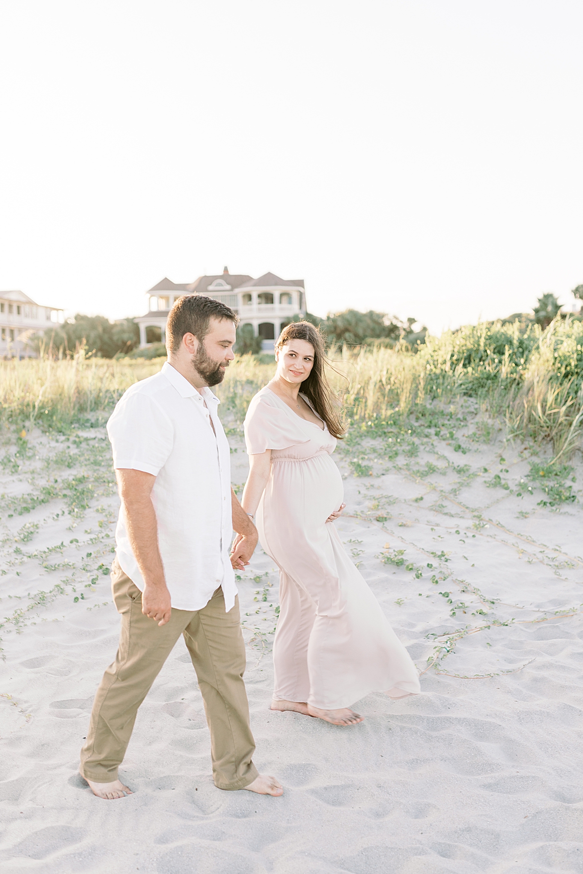 Couple walking along the dunes on Isle of Palms during sunset maternity session. Photos by Caitlyn Motycka Photography.