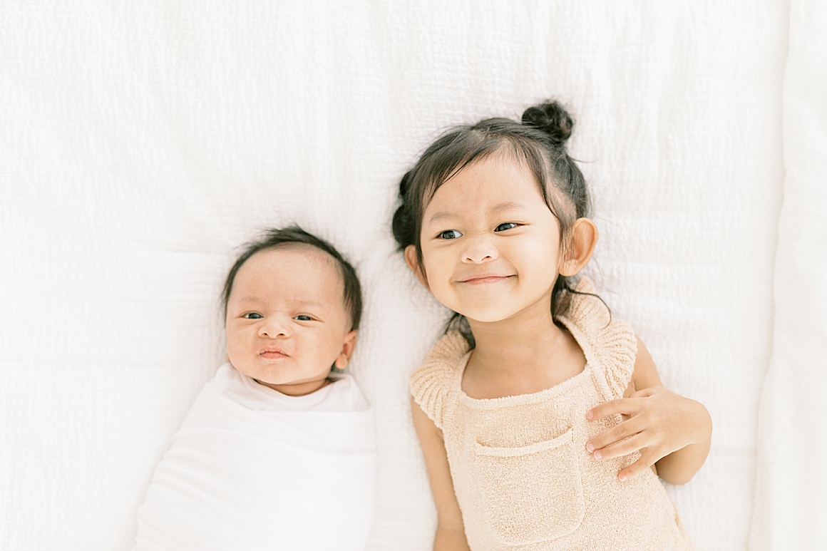 Baby boy and big sister laying on bed together for newborn photos. Photos by Caitlyn Motycka Photography.
