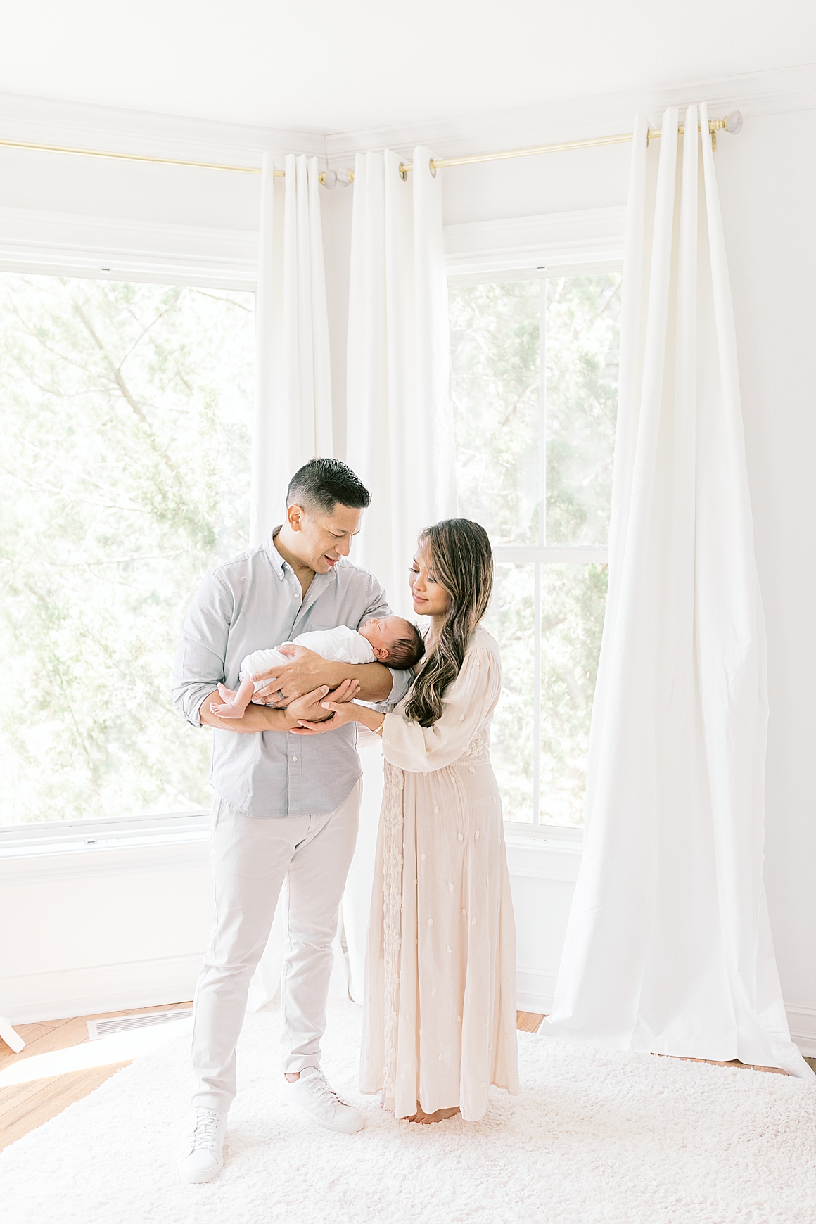 Mom and Dad standing in front of big windows in master bedroom for newborn session in Charleston, SC. Photos by Caitlyn Motycka Photography.