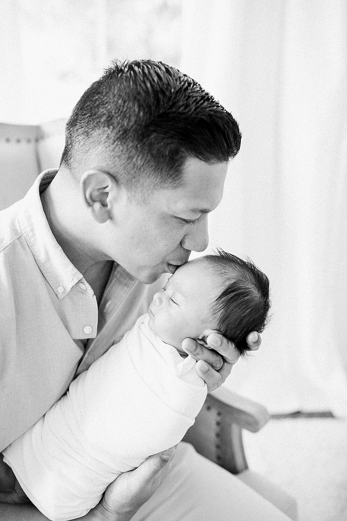 Black and white photo of Dad kissing newborn baby boy. Photos by Caitlyn Motycka Photography.