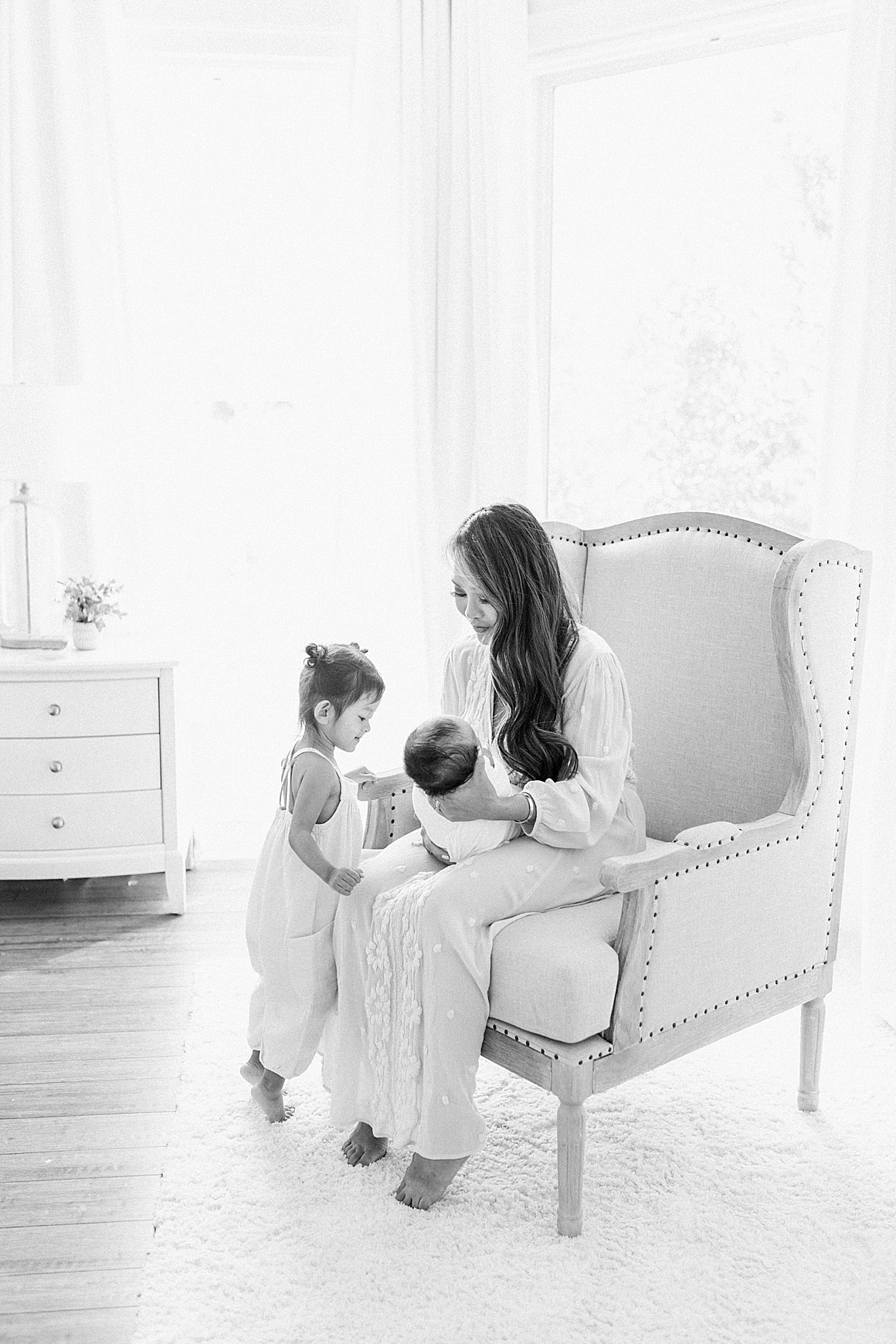 Black and white photo of Mom with her two children during newborn session in their home. Photos by Caitlyn Motycka Photography.