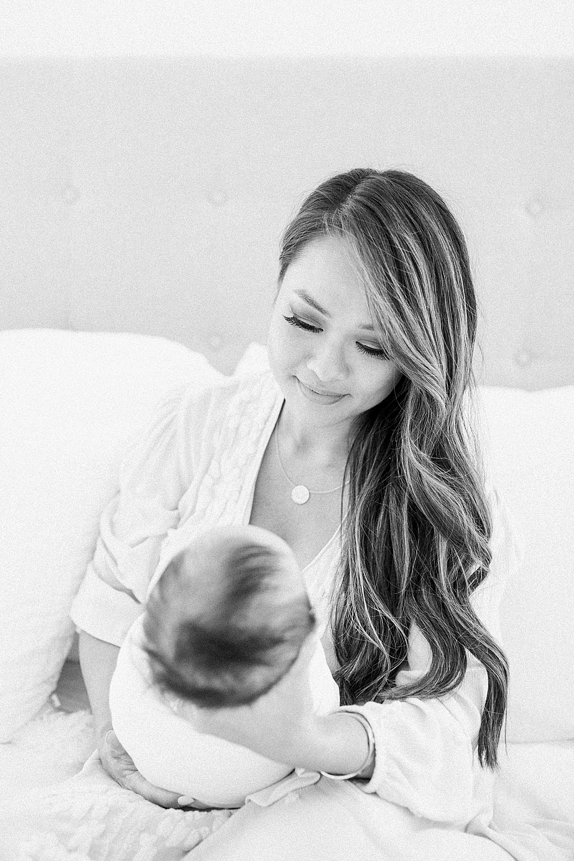 Black and white photo of Mom on bed with baby during in-home newborn session. Photos by Caitlyn Motycka Photography. 