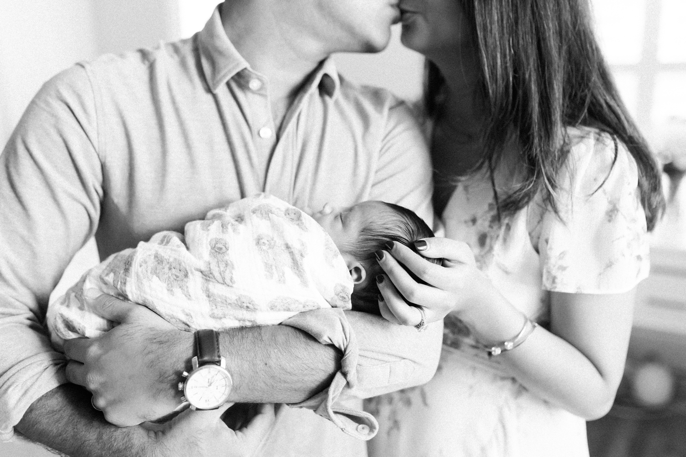 Mom and Dad kissing while holding their newborn son. Photo by Caitlyn Motycka Photography.