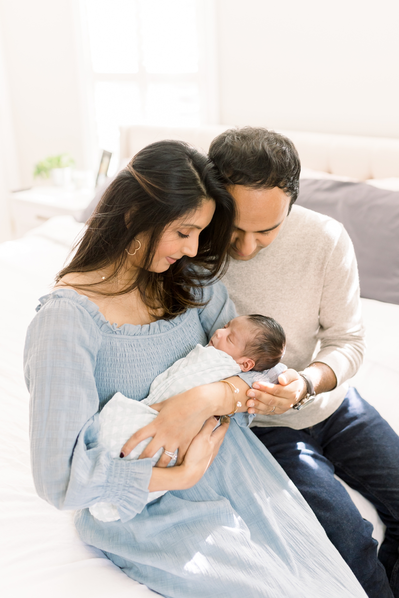 Mom and Dad sitting on bed with baby boy. Photo by Charleston Lifestyle Newborn Photographer, Caitlyn Motycka Photography.