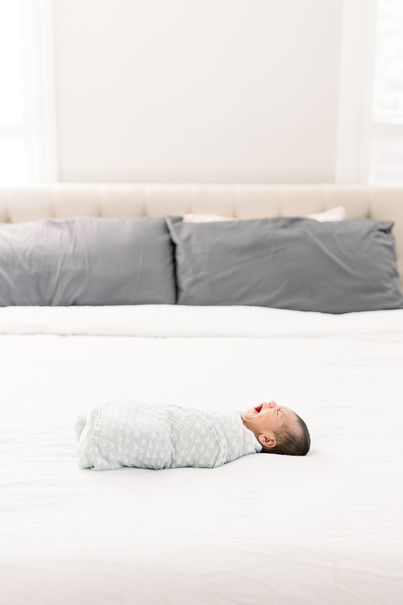 Lifestyle newborn photo of baby boy yawning. He's swaddled and laying on bed. Photo by Caitlyn Motycka Photography.