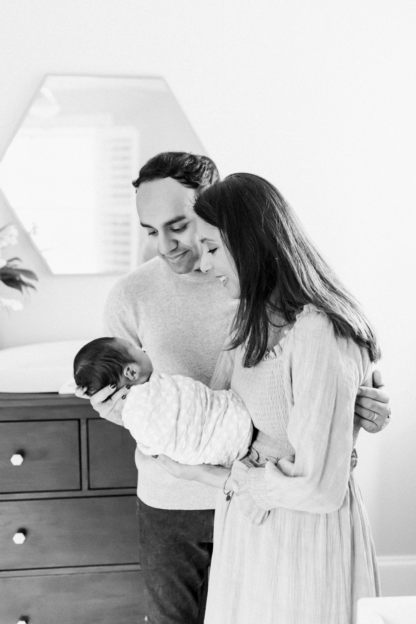 Black and white photo of Mom, Dad and baby boy during in-home lifestyle newborn session. Photo by Caitlyn Motycka Photography.
