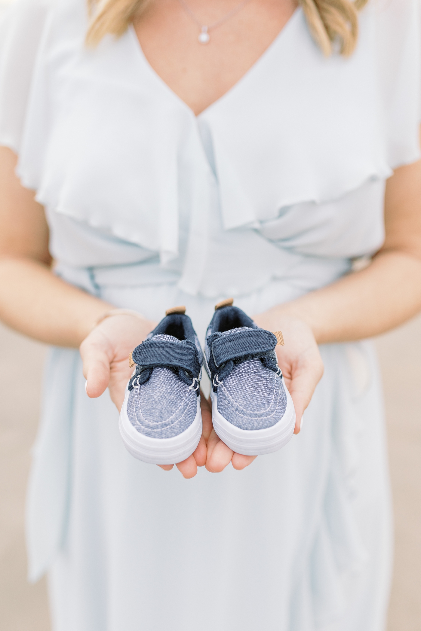 Gender reveal photo of Mom holding blue baby shoes. Photo by Caitlyn Motycka Photography.