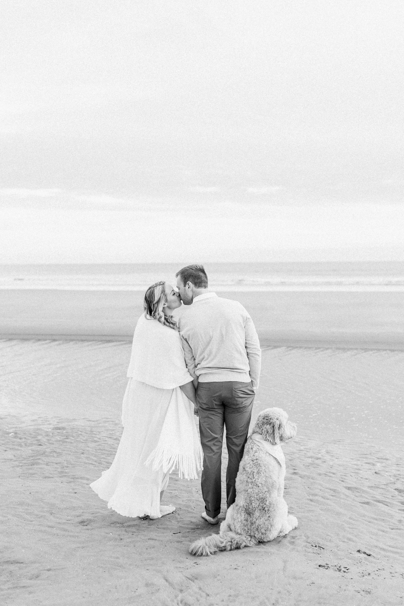 Black and white photo on the beach with couple and dog. Photo by Caitlyn Motycka Photography.