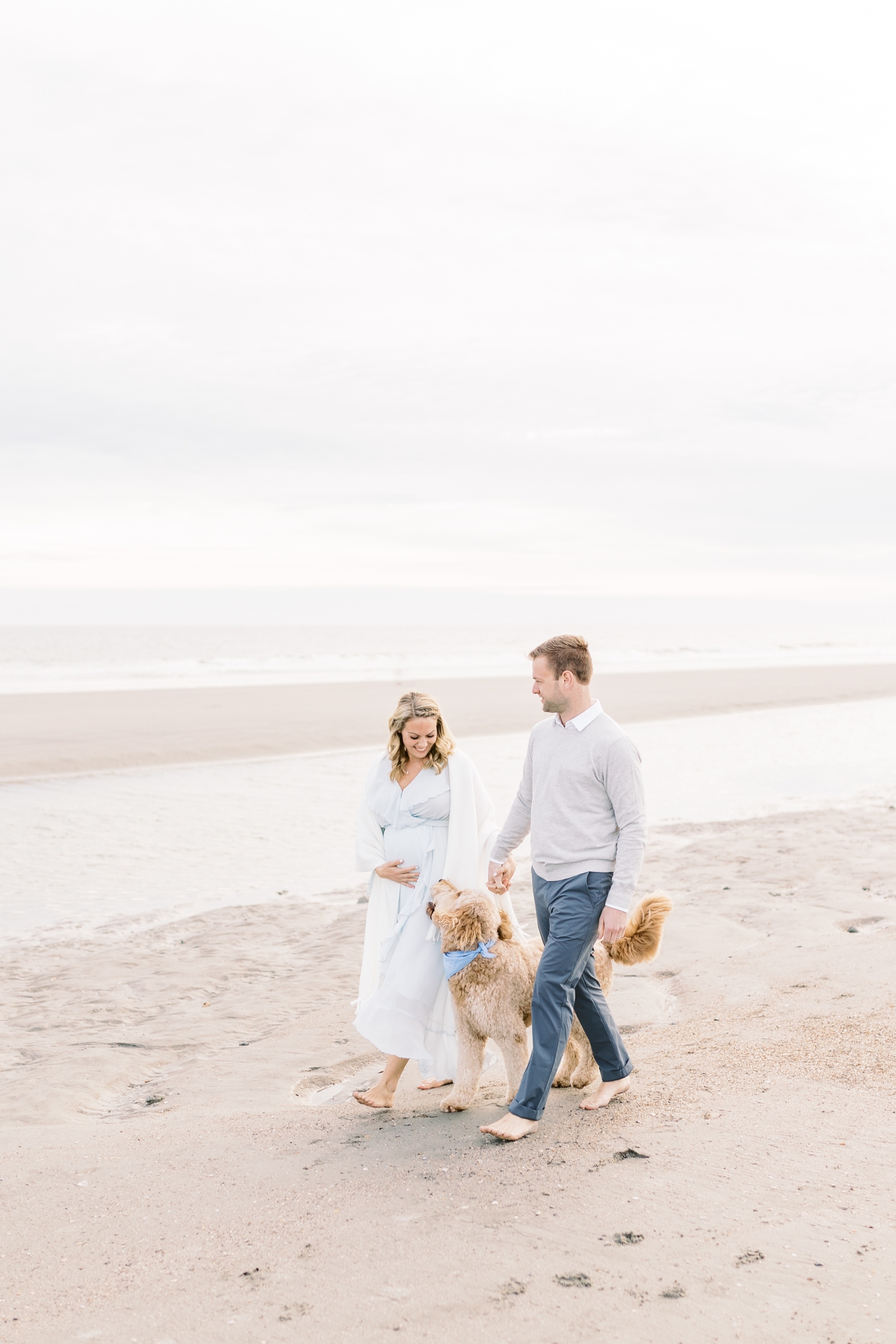 Couple walking on the beach with Goldendoodle. Photos by Caitlyn Motycka Photography.