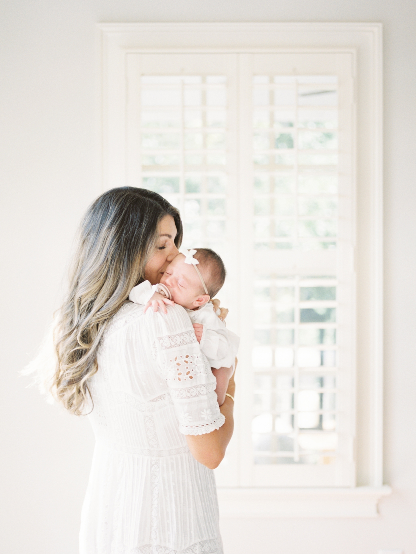 Newborn session image on film of Mom kissing baby girl. Photo by Caitlyn Motycka Photography.