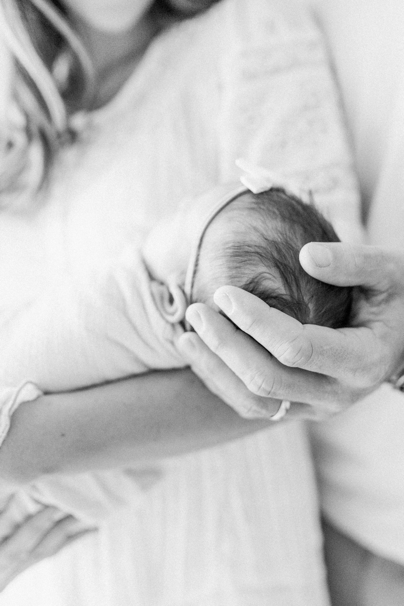 Black and white image of Dad's hand on baby's head. Photo by Caitlyn Motycka Photography.