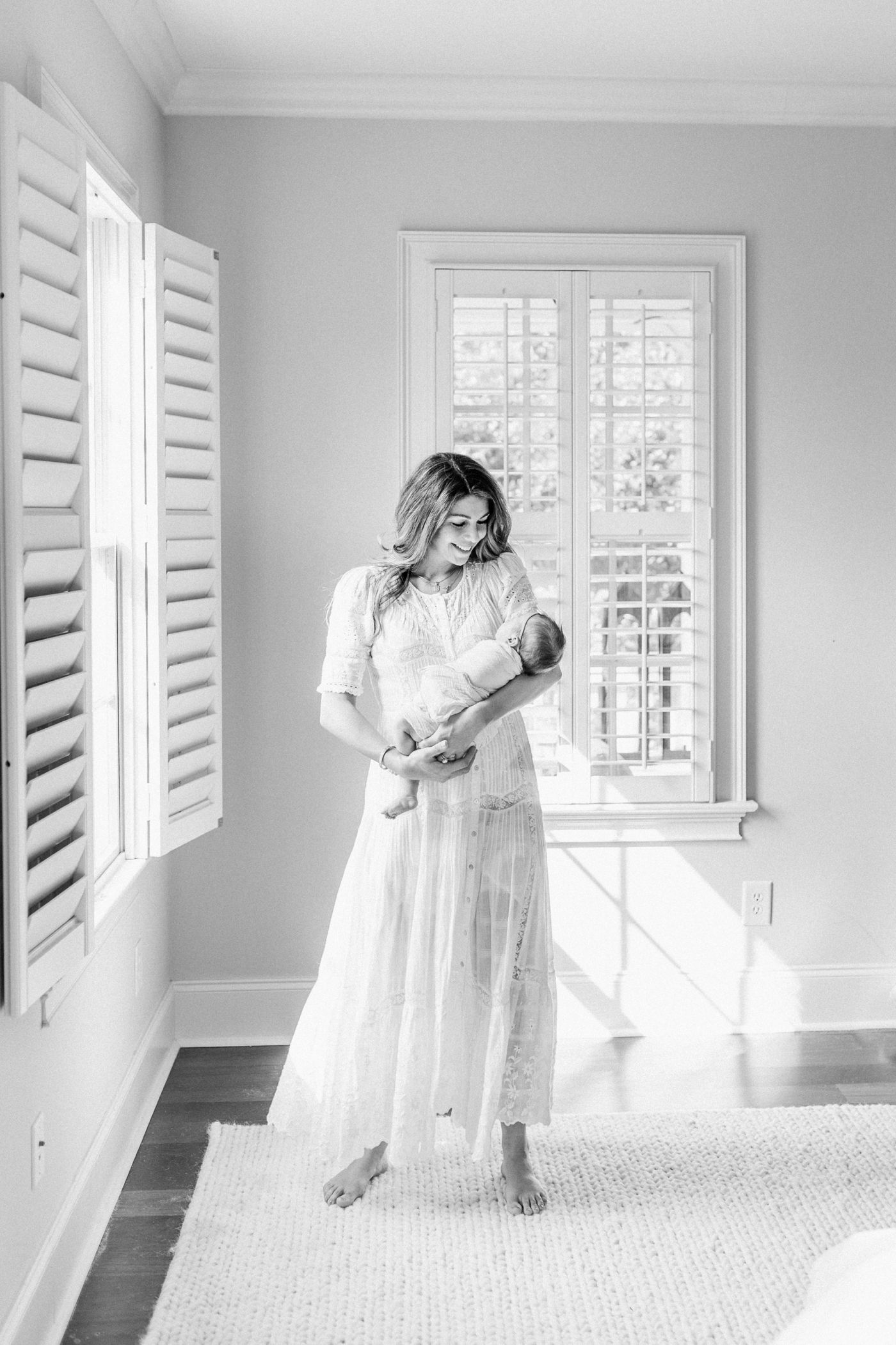 Black and white image of Mom rocking baby girl while window light shines on them. Photo by Mount Pleasant newborn photographer, Caitlyn Motycka Photography.