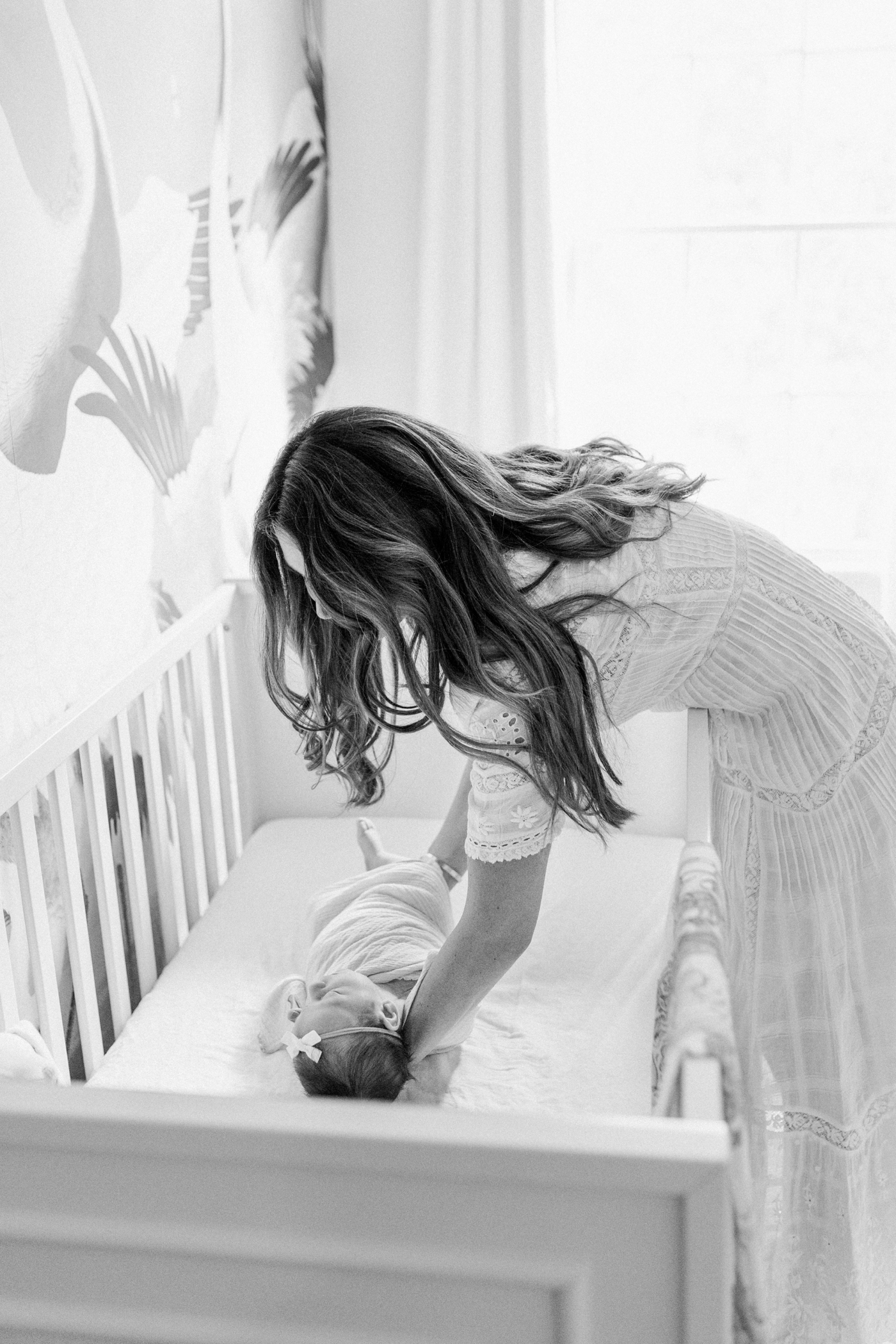 Black and white image of Mom placing baby girl in crib during lifestyle newborn session. Photo by Caitlyn Motycka Photography.