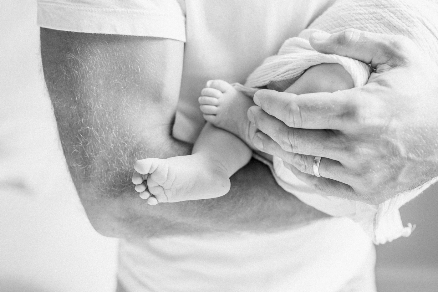 Black and white closeup image of baby's feet in Dad's arms. Photo by Caitlyn Motycka Photography.