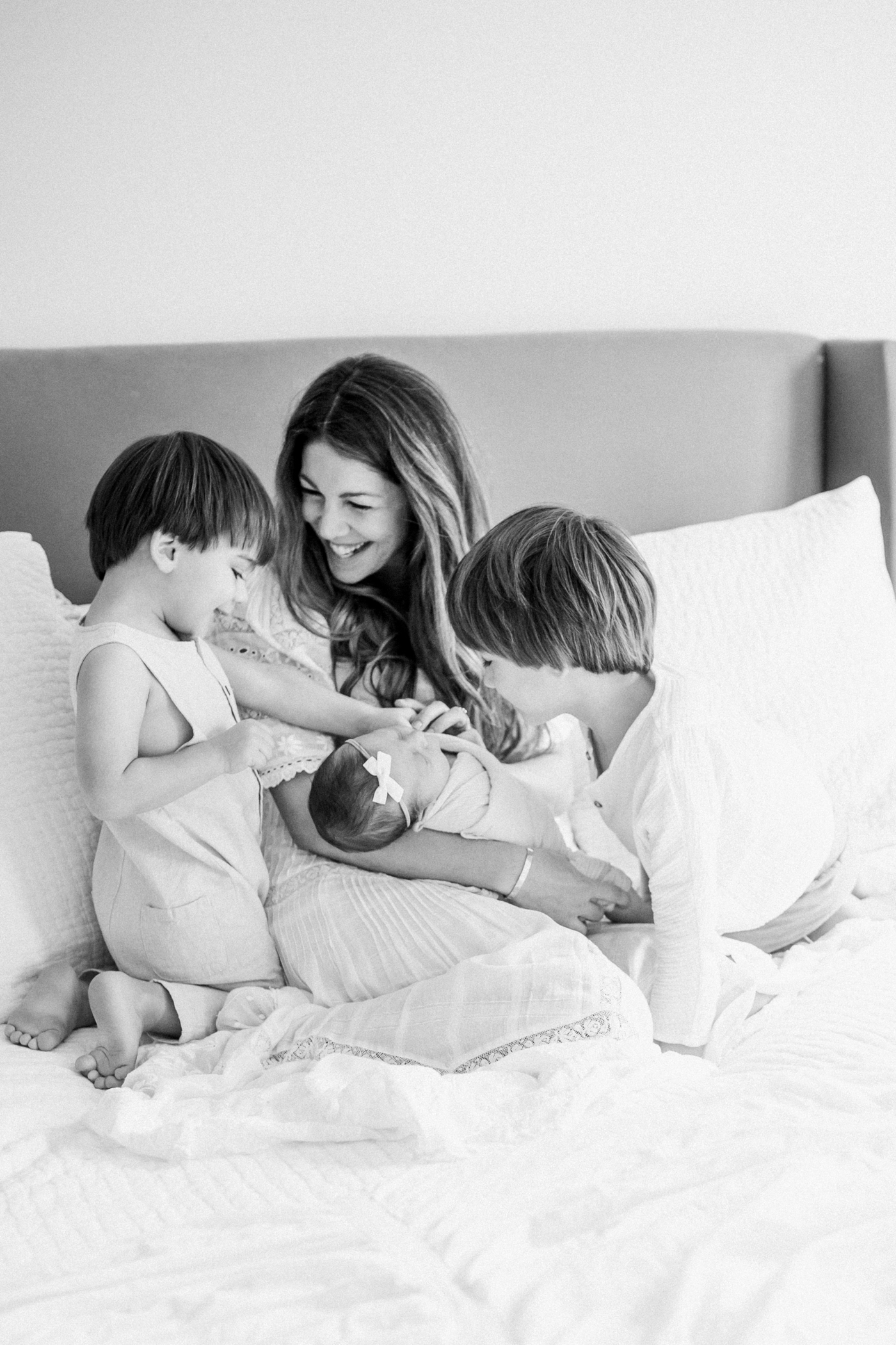 Stunning black and white image of Mom holding baby and big brothers smiling at her. Photo by Caitlyn Motycka Photography.
