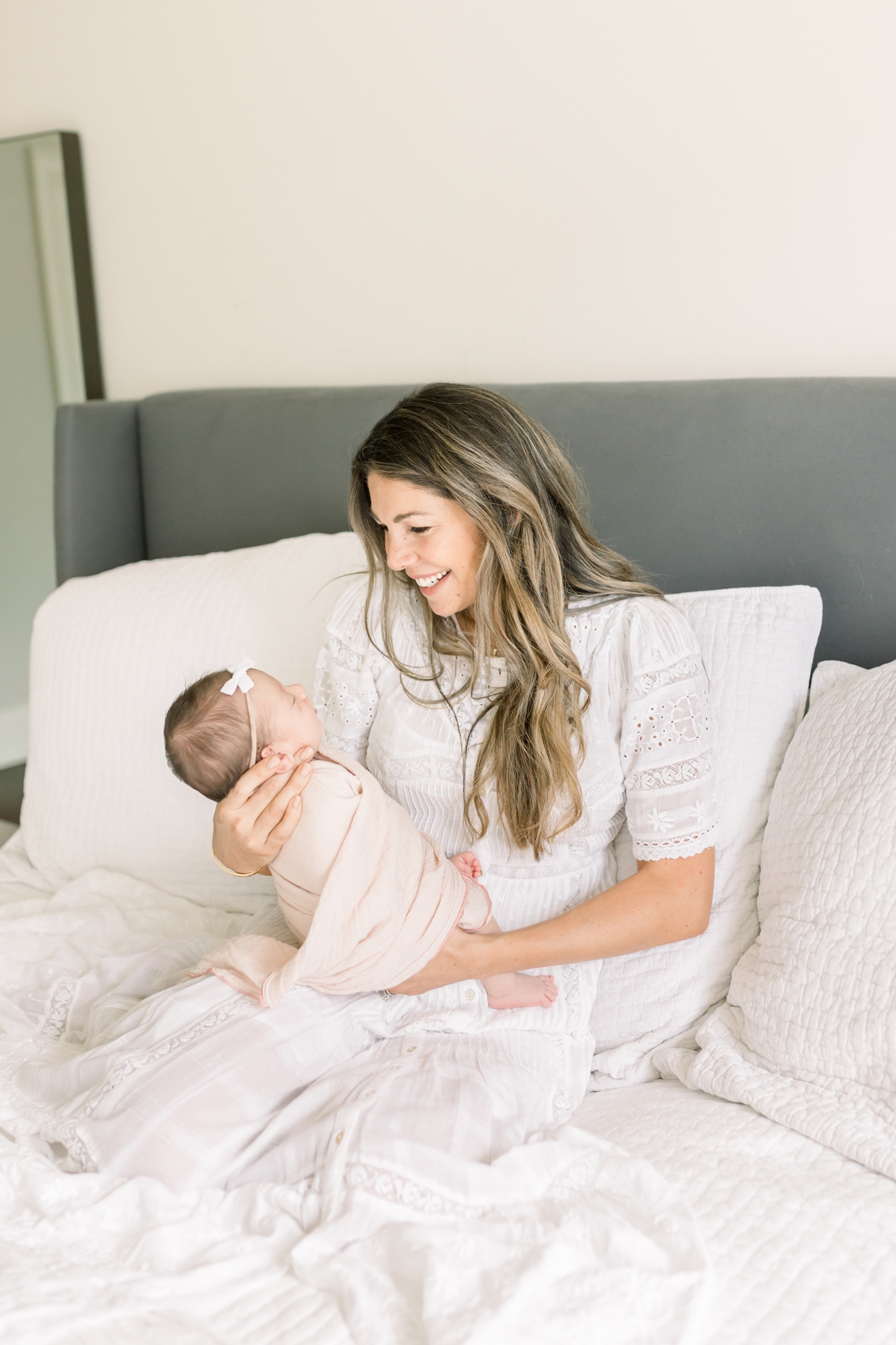Mom holding baby girl in light pink swaddle on bed during newborn session. Photo by Caitlyn Motycka Photography.