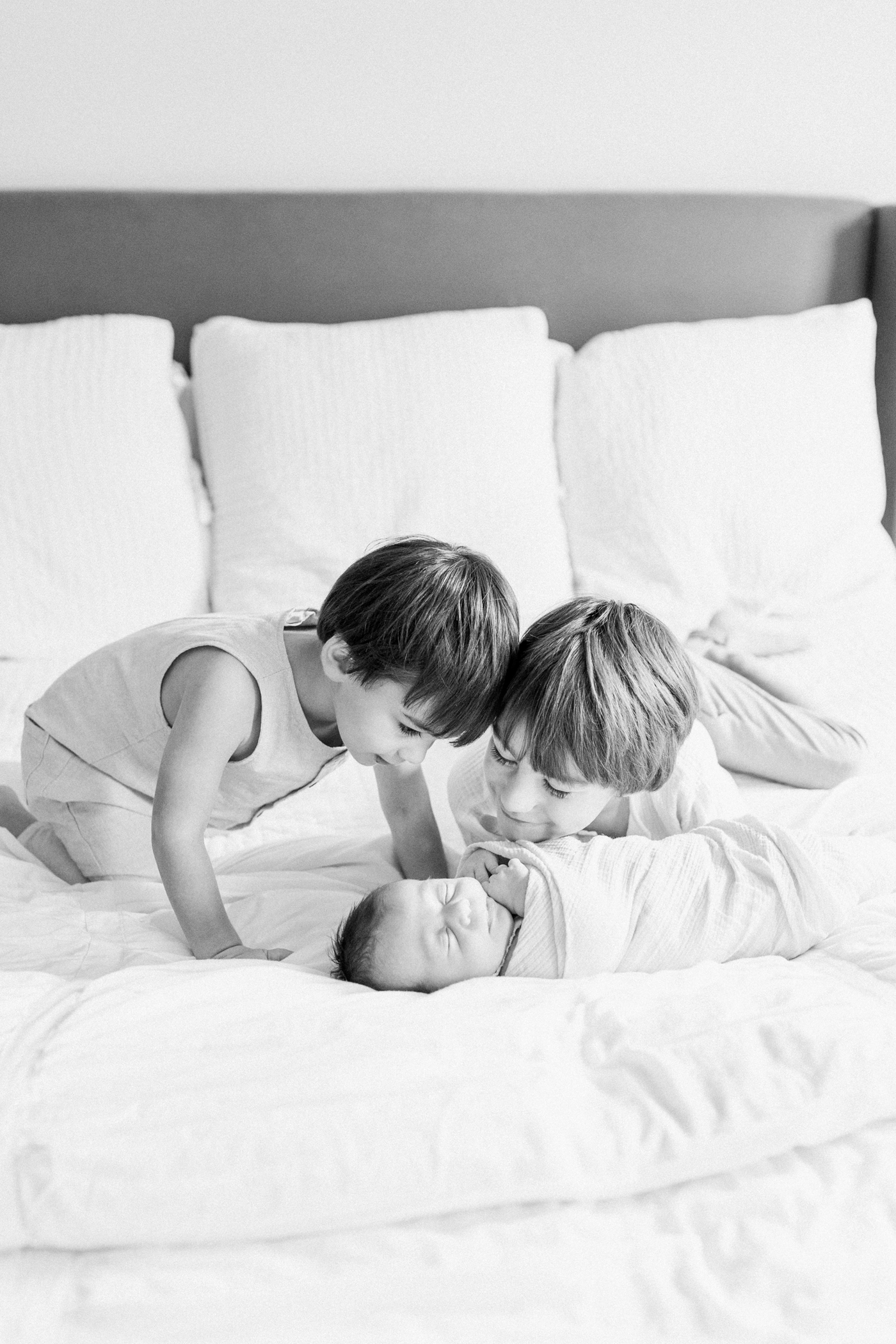 Black and white image of two older siblings looking at their baby sister. Photo by Mt Pleasant newborn photographer, Caitlyn Motycka Photography.