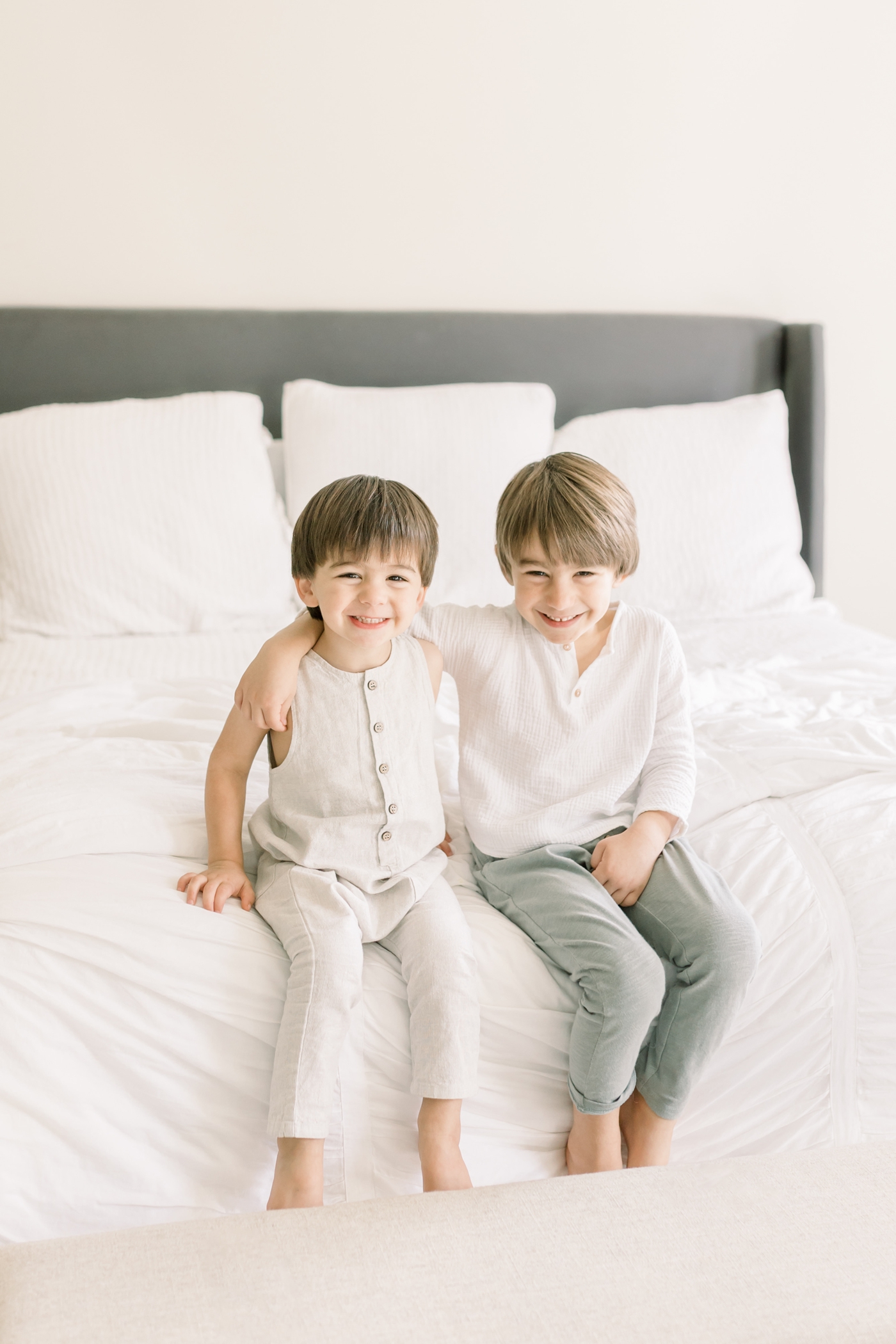 Proud big brothers sitting on the bed during newborn session. Photo by Caitlyn Motycka Photography.
