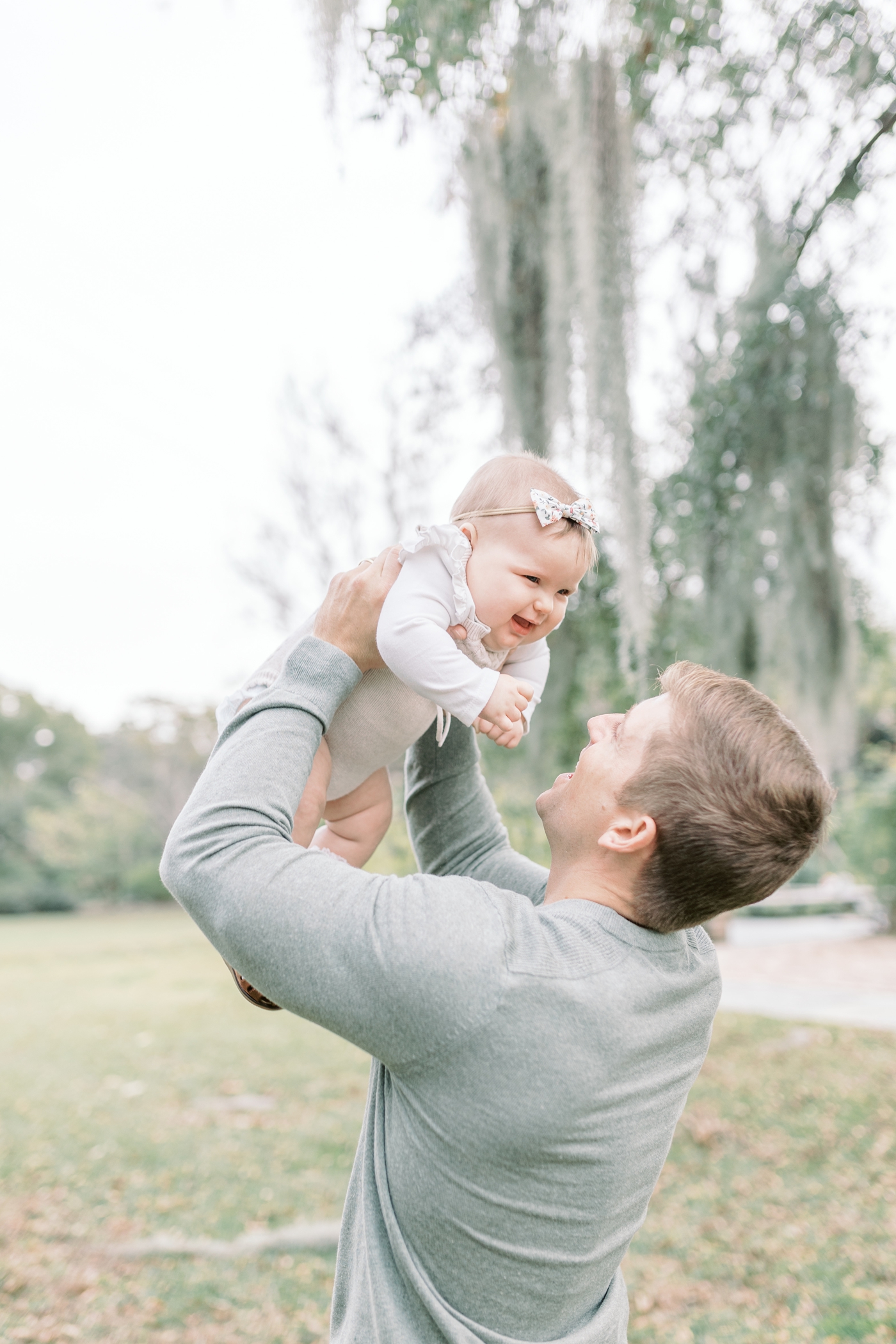 Dad playing airplane with baby during family photoshoot at Hampton Park. Photo by Caitlyn Motycka Photography.