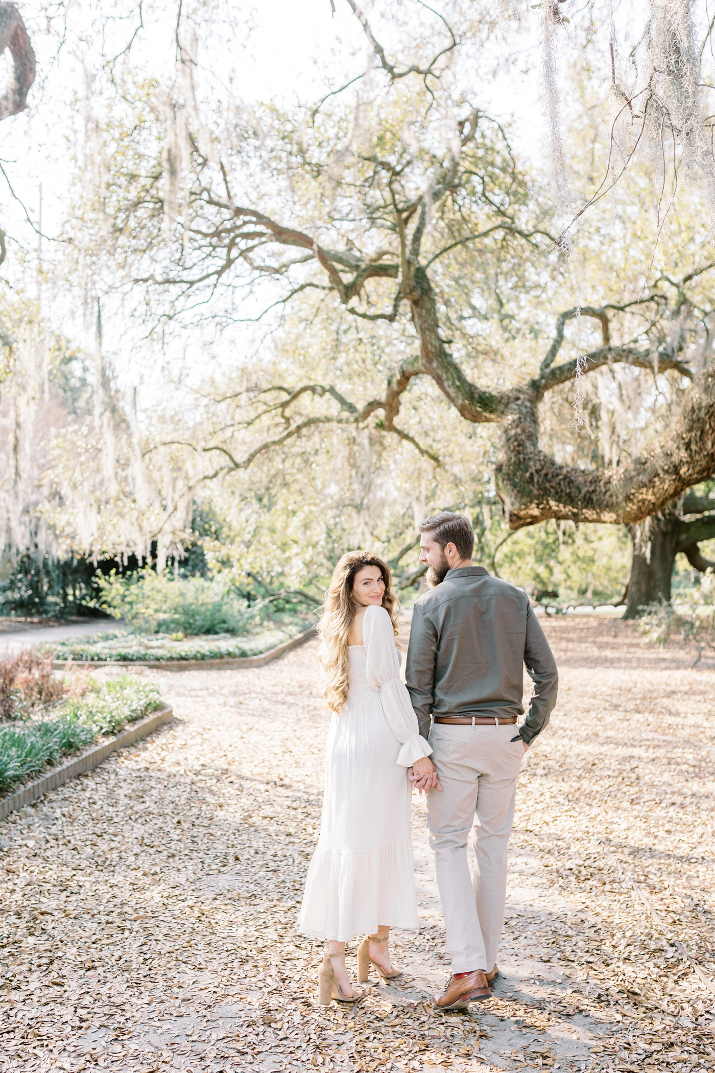 Portrait of husband looking lovingly at wife as they walk away under big oak trees in Charleston maternity session. Photo by Caitlyn Motycka Photography.