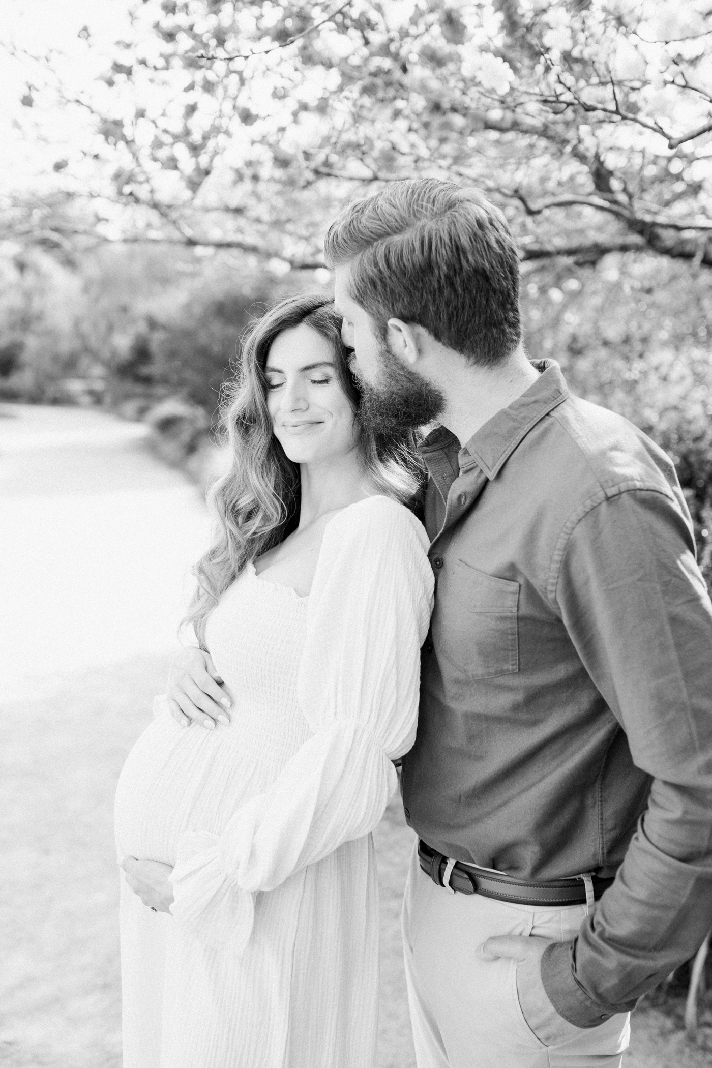 Black and white image of Dad kissing Mom in park maternity session by hybrid fine art photographer, Caitlyn Motycka Photography.