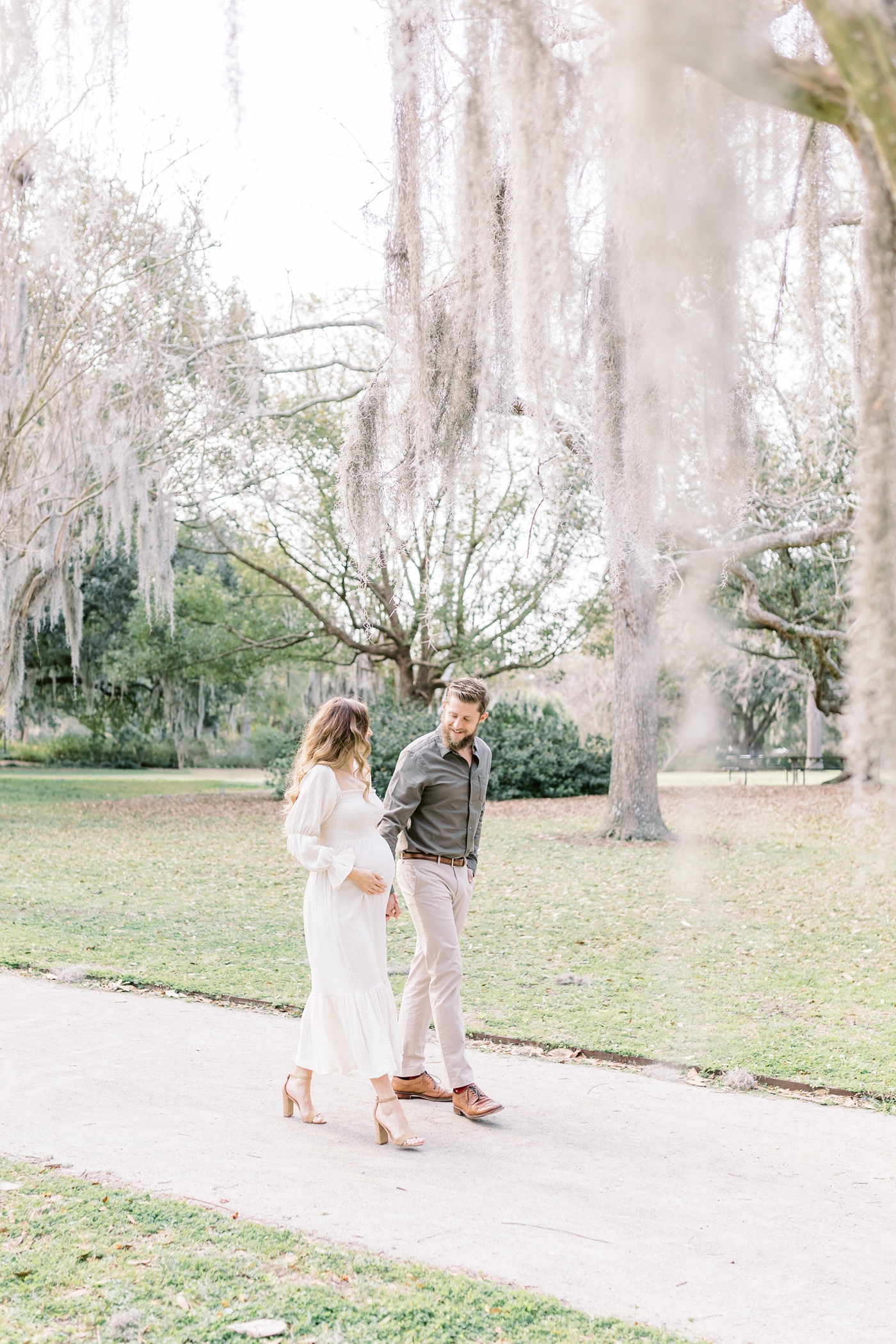 Expecting parents walking under the spanish moss at Hampton Park. Photo by Charleston fine art maternity photographer, Caitlyn Motycka Photography.