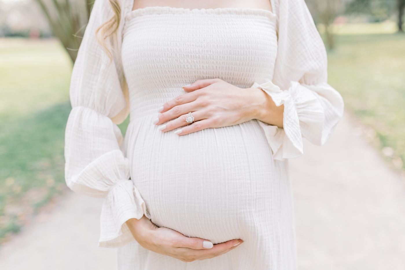 Closeup of baby bump with mom in white maternity dress. Photo by Caitlyn Motycka Photography.