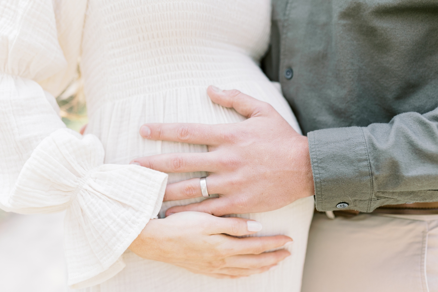 Closeup of baby bump with husband's hand on bump. Photo by Caitlyn Motycka Photography.