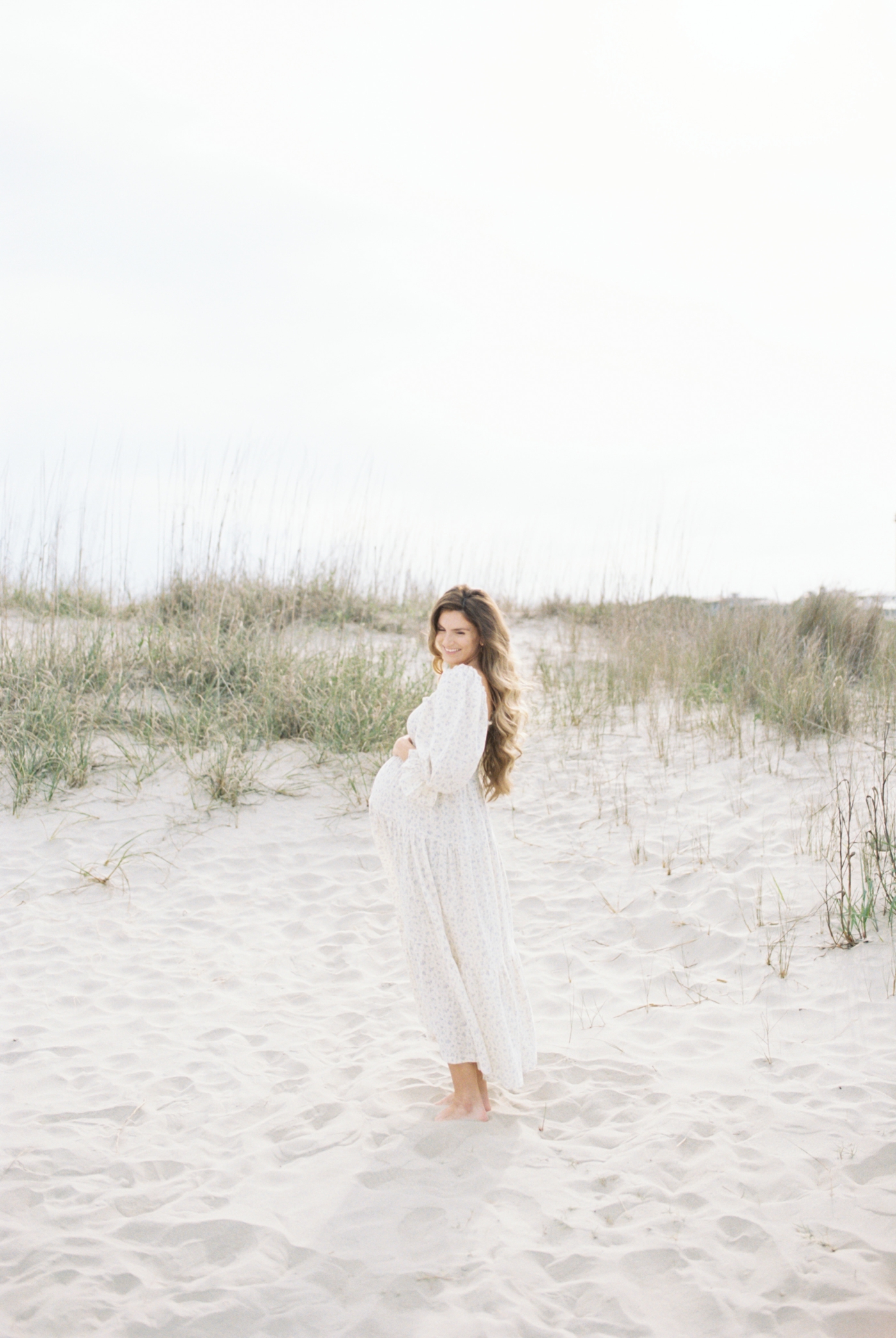 Pregnant woman in flowy dress on the beach | Photo by Caitlyn Motycka Photography.