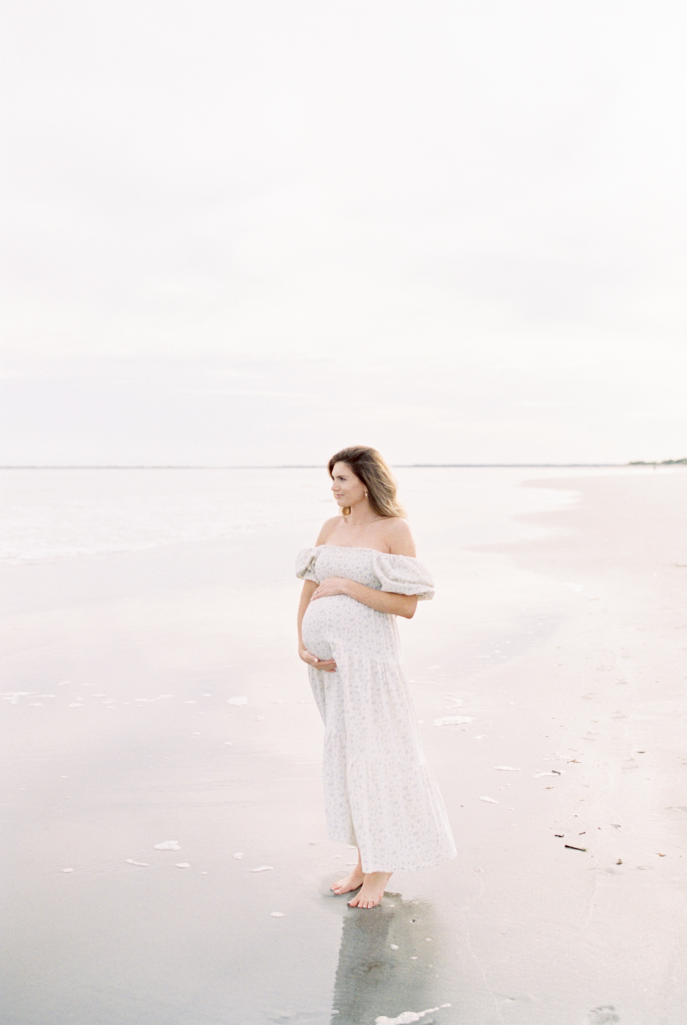 Mother to be cradling her belly looking out at the ocean | Photo by Caitlyn Motycka Photography.