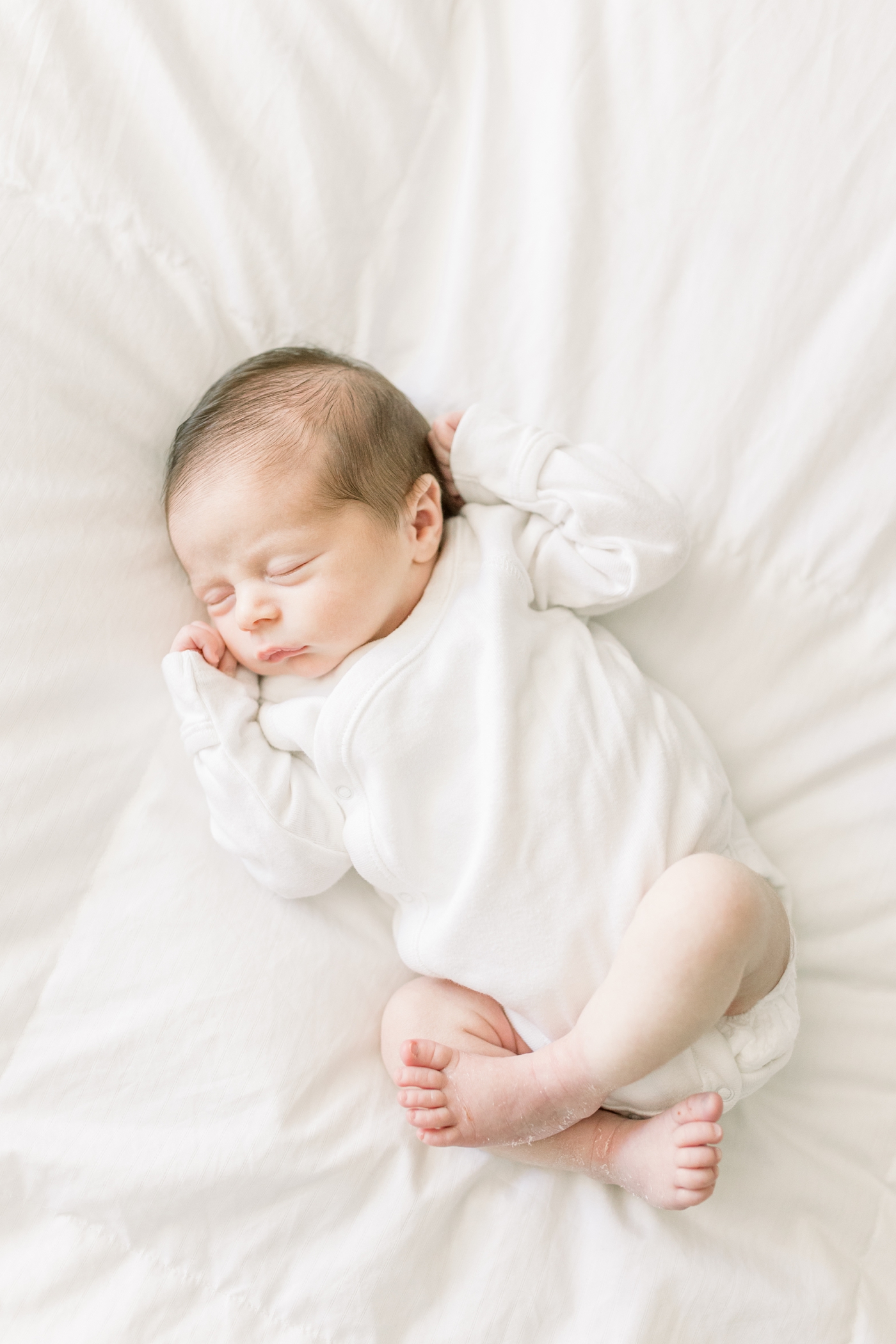 Newborn baby sleeping in a white onesie | Photo by Caitlyn Motycka Photography.